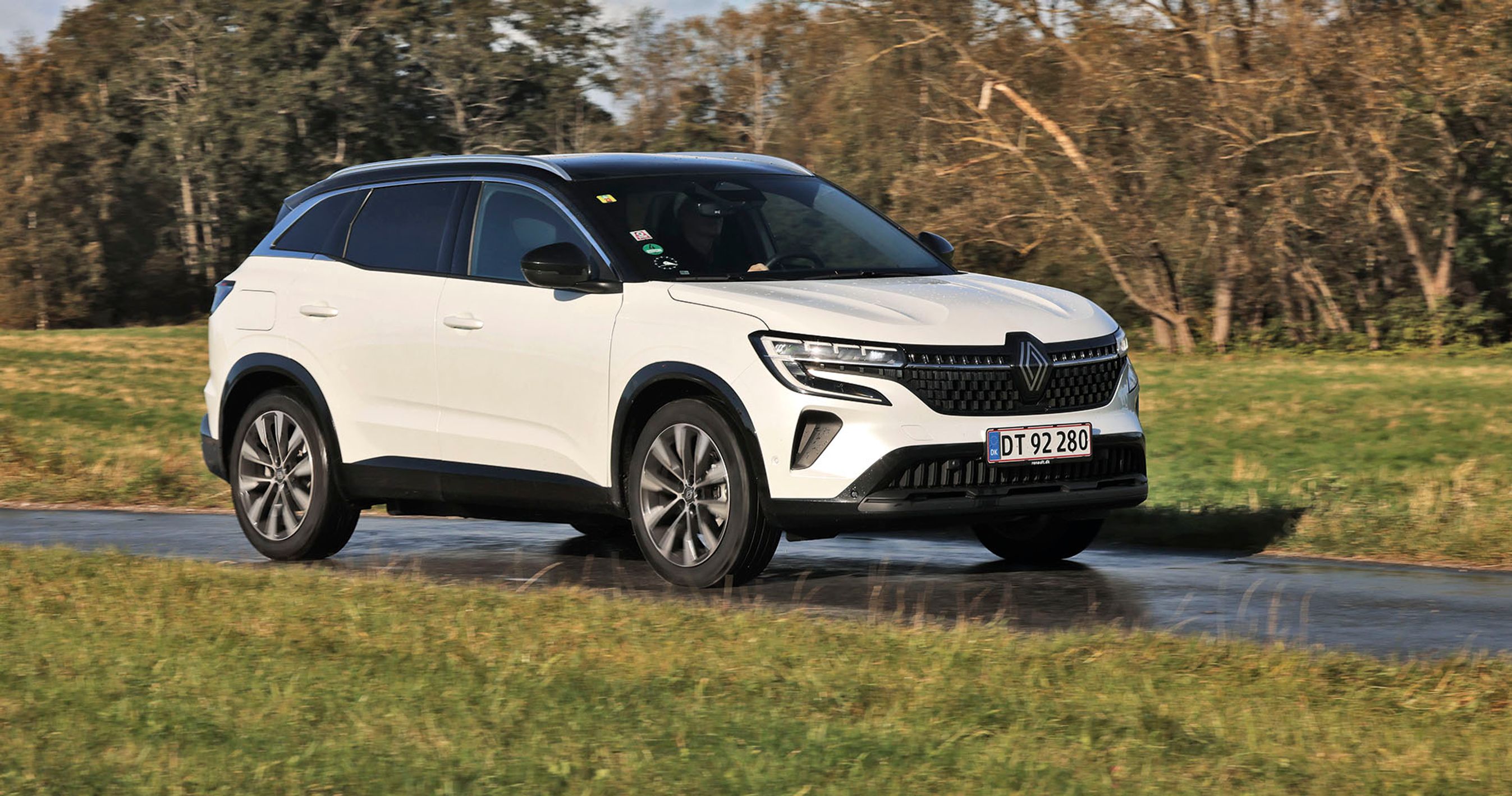 En hvid Renault Austral kører på en landevej med træer i baggrunden