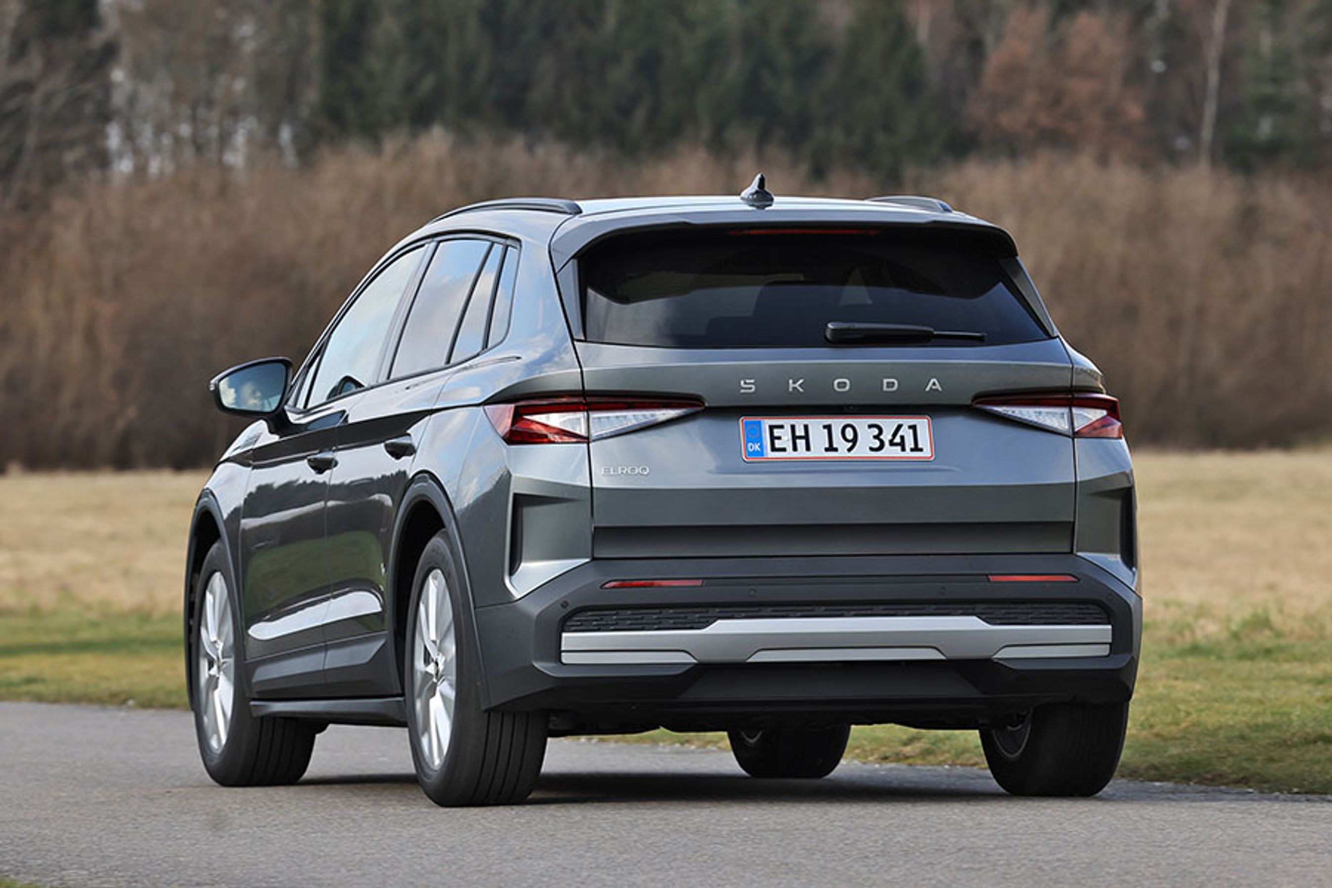 Skoda Elroq 50 set bagfra, mens den kører på en landevej med træer og marker i baggrunden