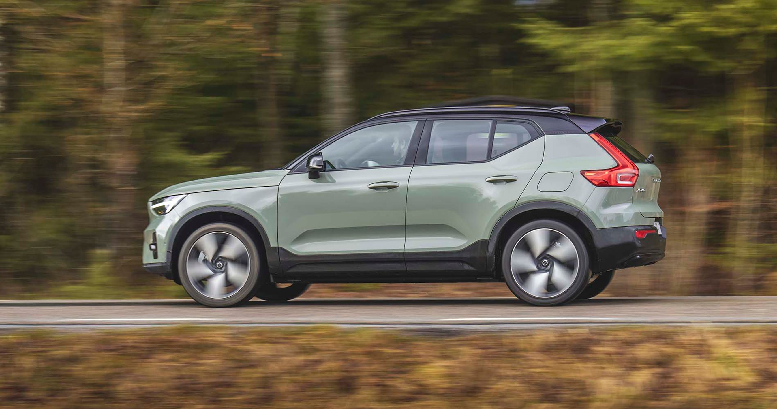 En grøn Volvo XC40 kører på en landevej med træer i baggrunden