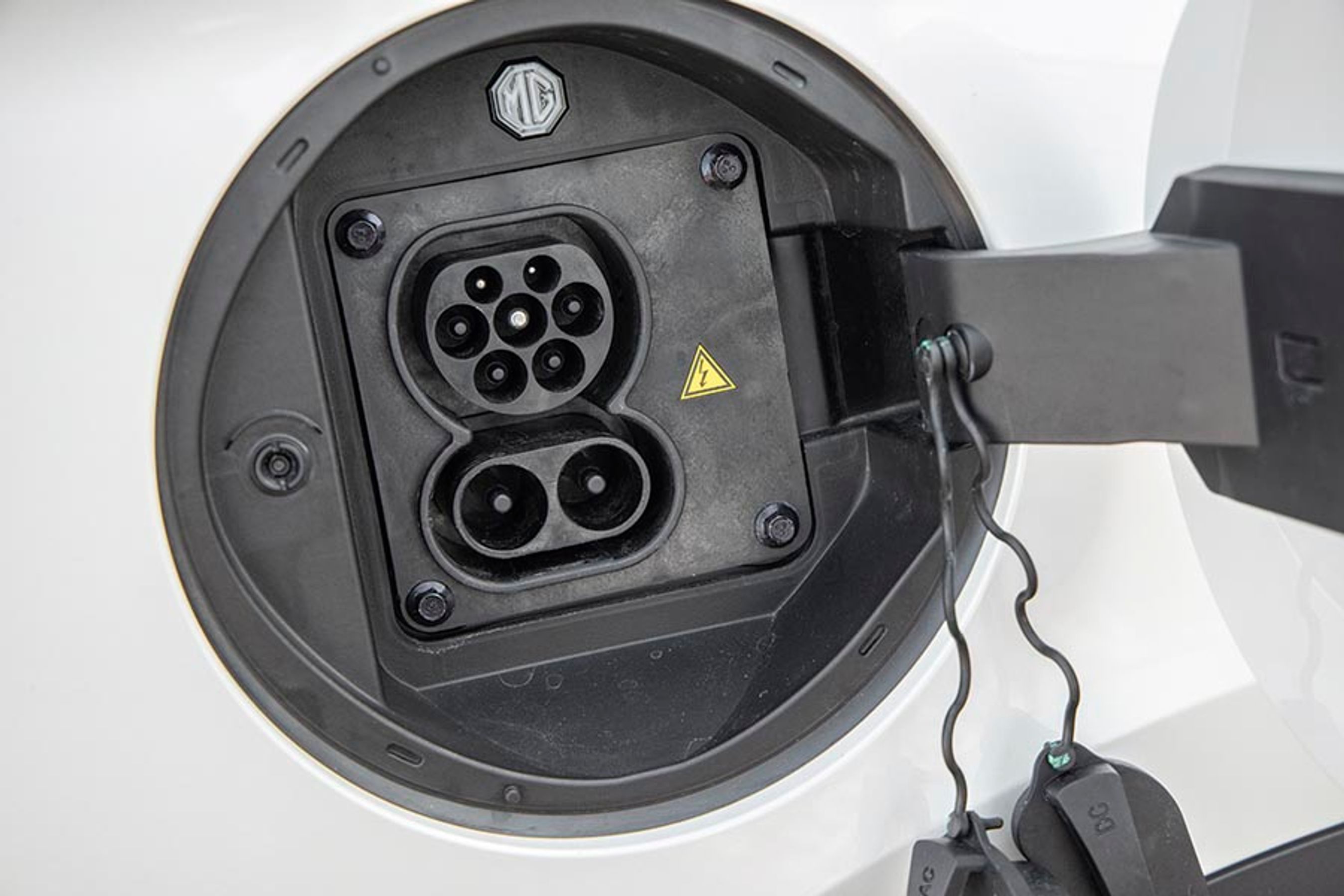 Ladelugen er placeret ved højre baghjul, og under dækslet er der to gummipropper, der skal fjernes, før man kan lade. Der er kontrollys, men vi savner orienteringslys og en knap til frigørelse af kablet. Bilen kan lade med op til 92 kW på farten med DC-Combo-stikket, og hjemme med 11 kW via en trefaset ladeboks.