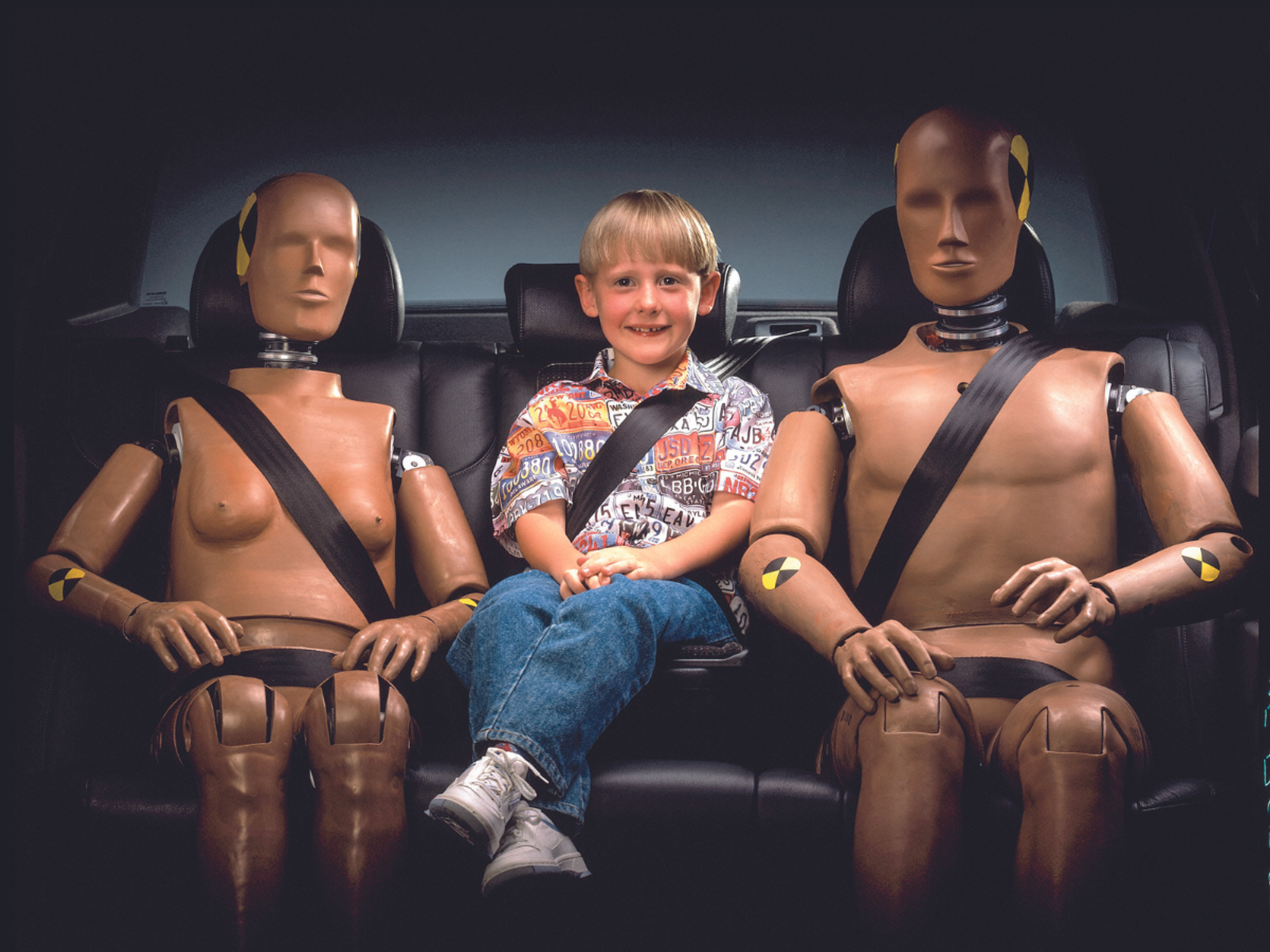 Kvindelig og mandlig chrashtestdukke i bil med et menneskebarn i mellem dem