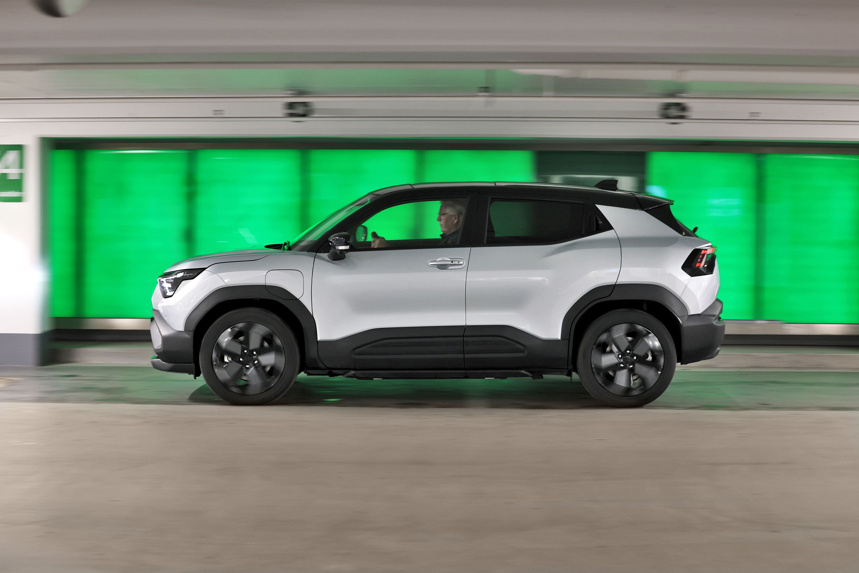 Suzuki eVitara set fra siden, mens den kører foran grøn baggrund