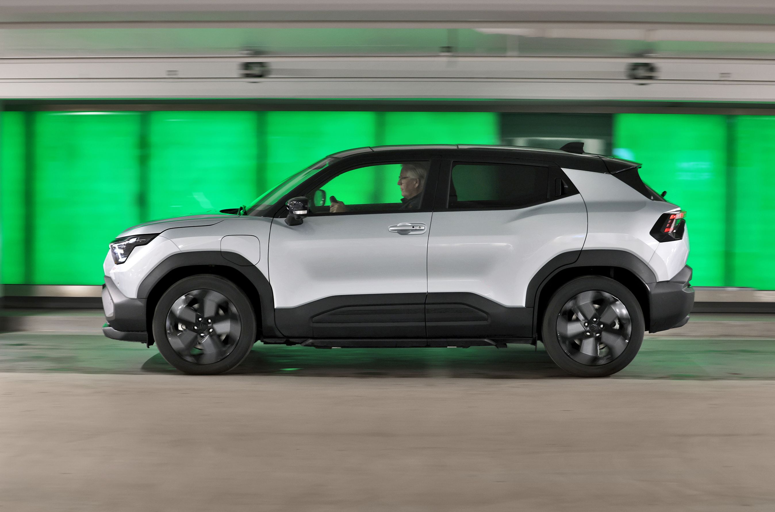 Suzuki eVitara set fra siden, mens den kører foran grøn baggrund