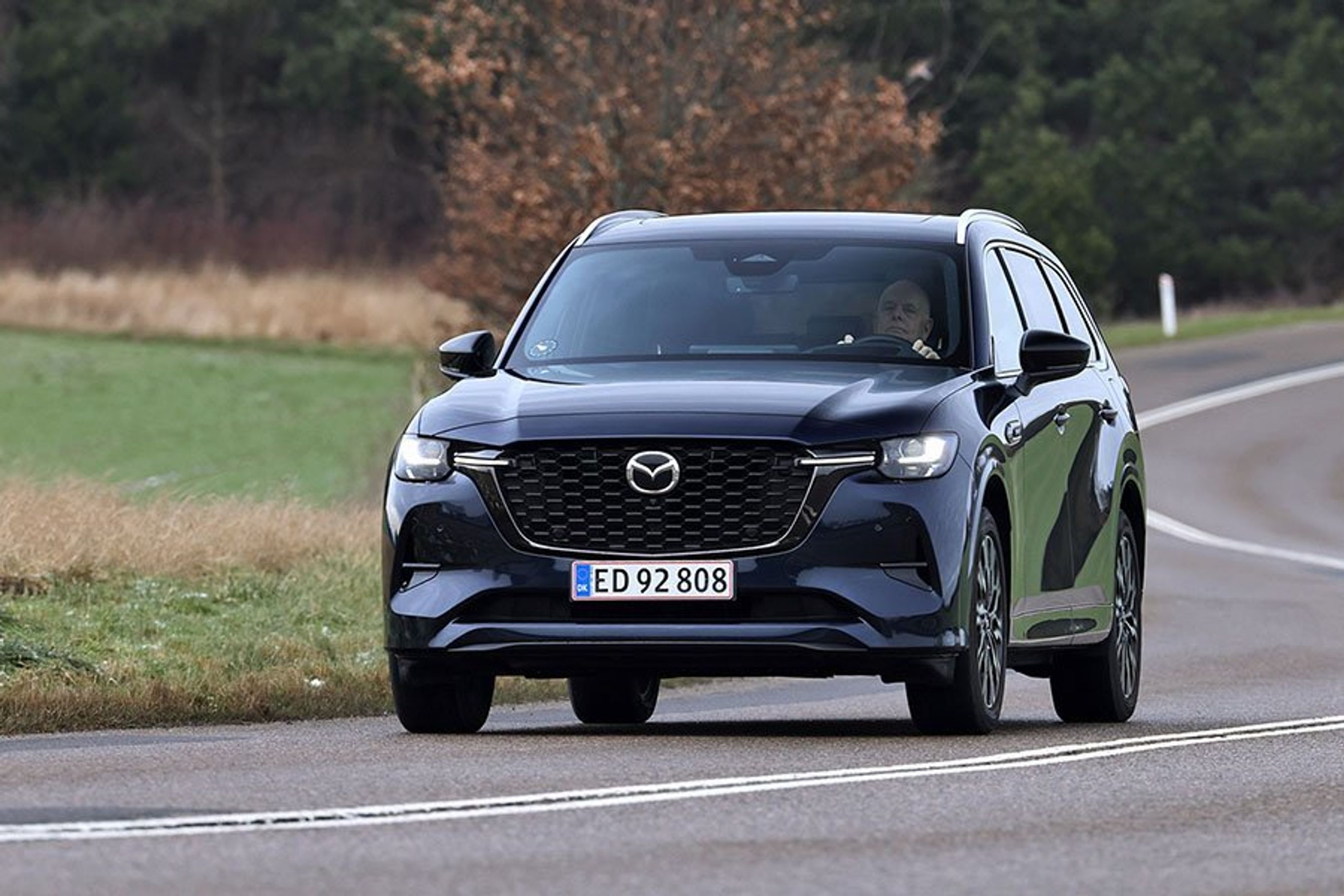 Mazda CX-80 set forfra, mens den kører ud af sving på landevej