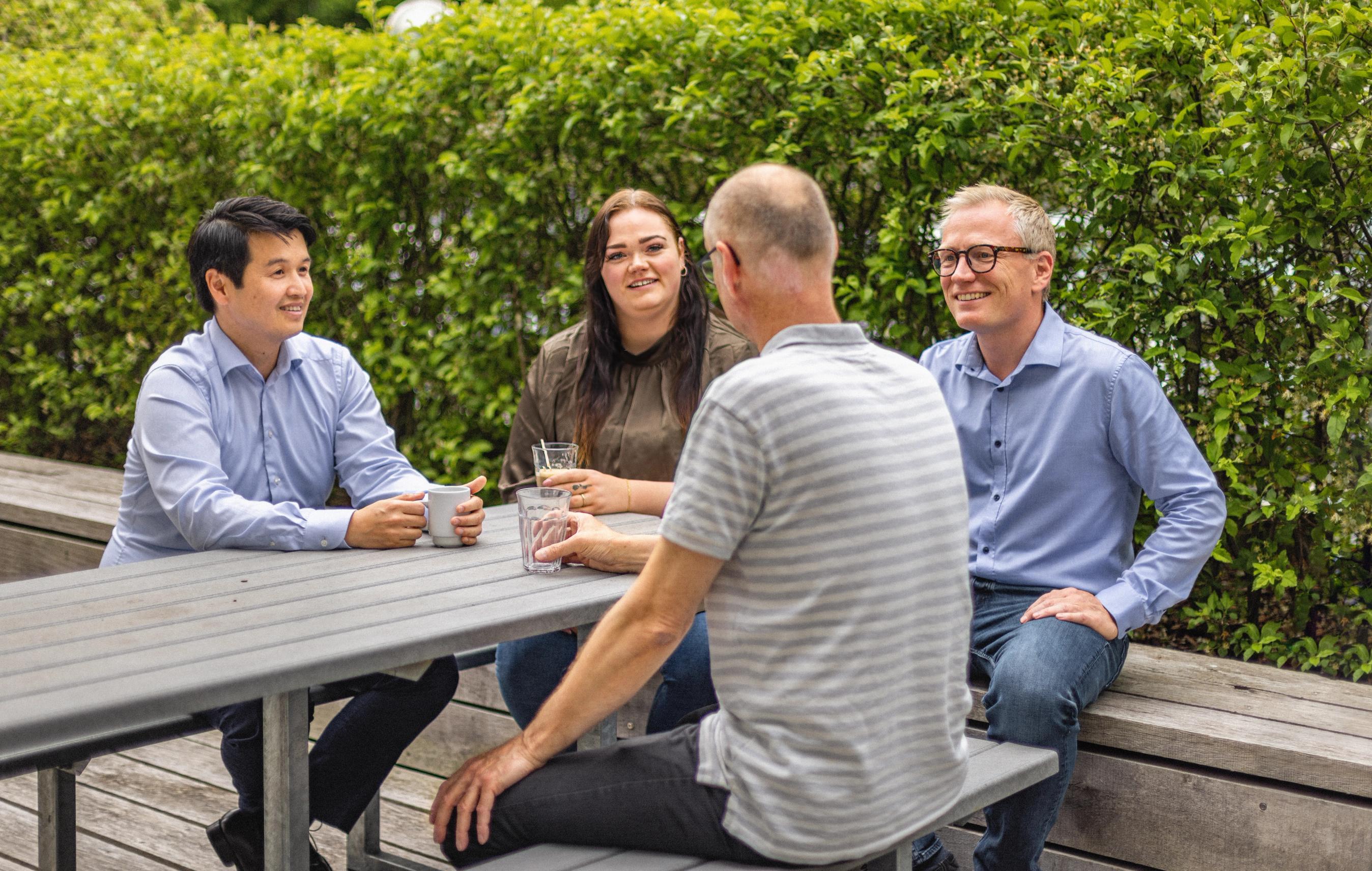 Fire personer på en bænk drikker kaffe sammen udenfor