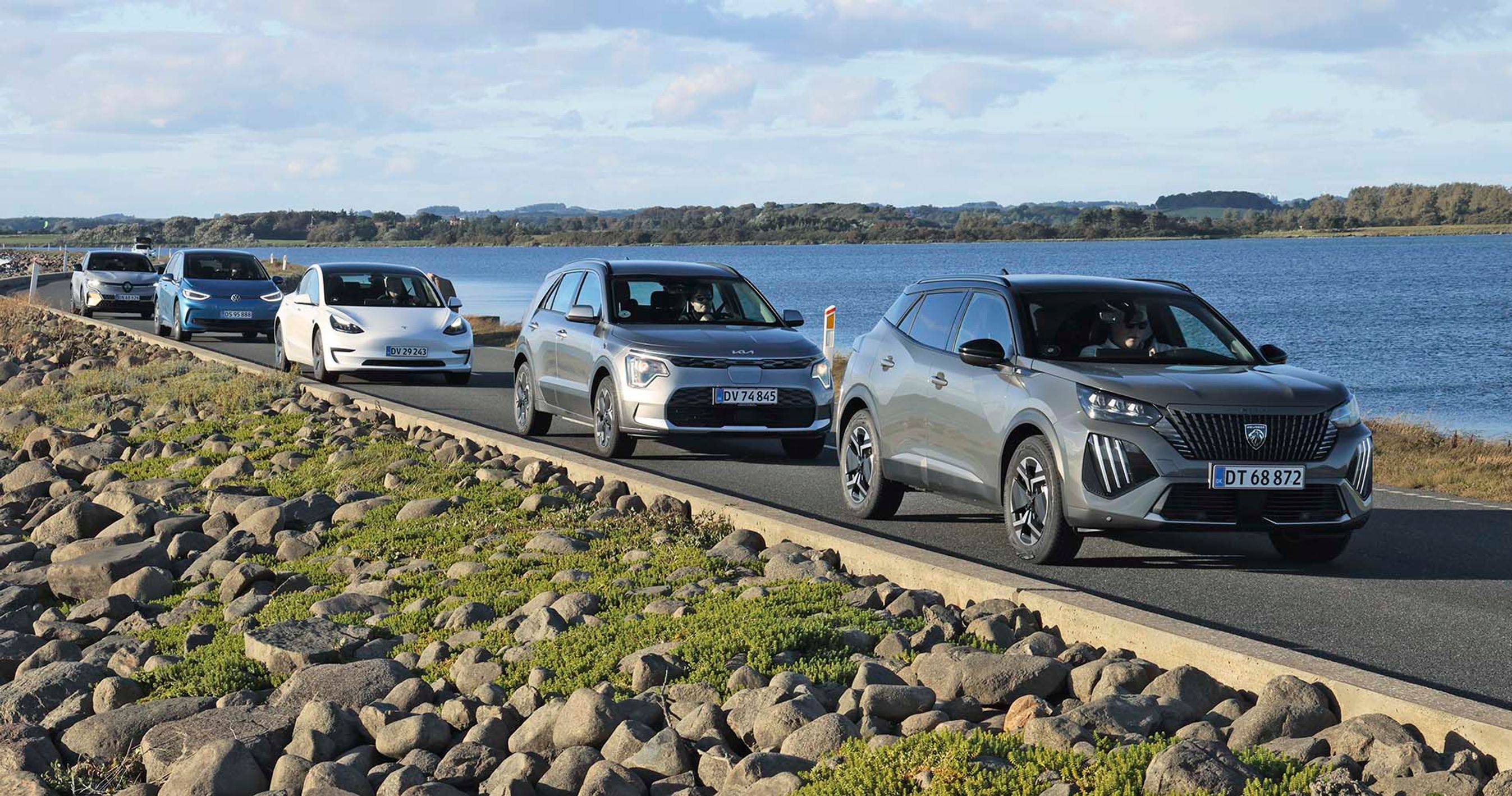 Fem elbiler kører på en vej med hav på begge sider