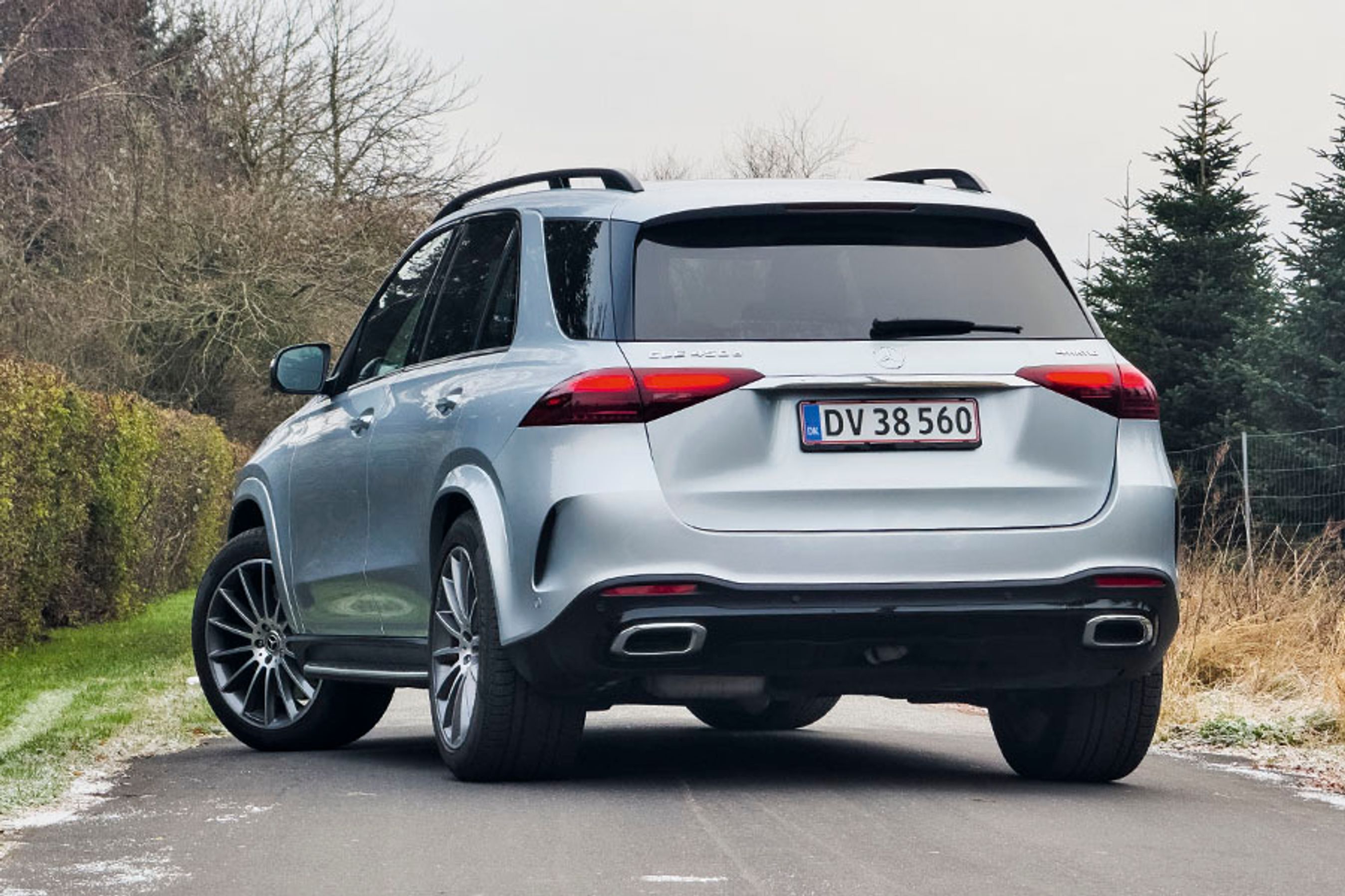 En sølvgrå Mercedes-Benz GLE set bagfra, mens den holder på en vej med en hæk i baggrunden.
