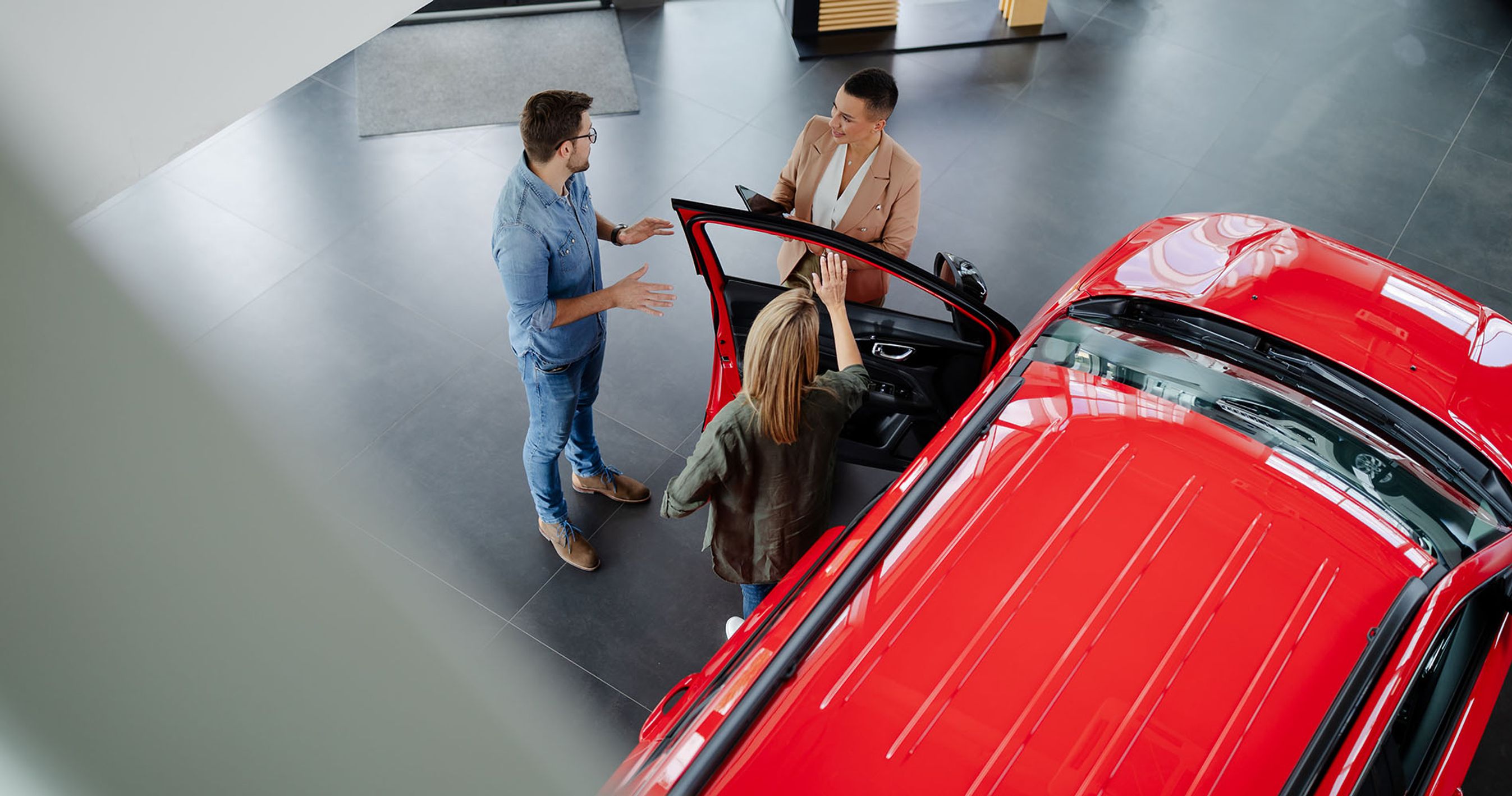 Bilsælger viser rød bil frem til to personer