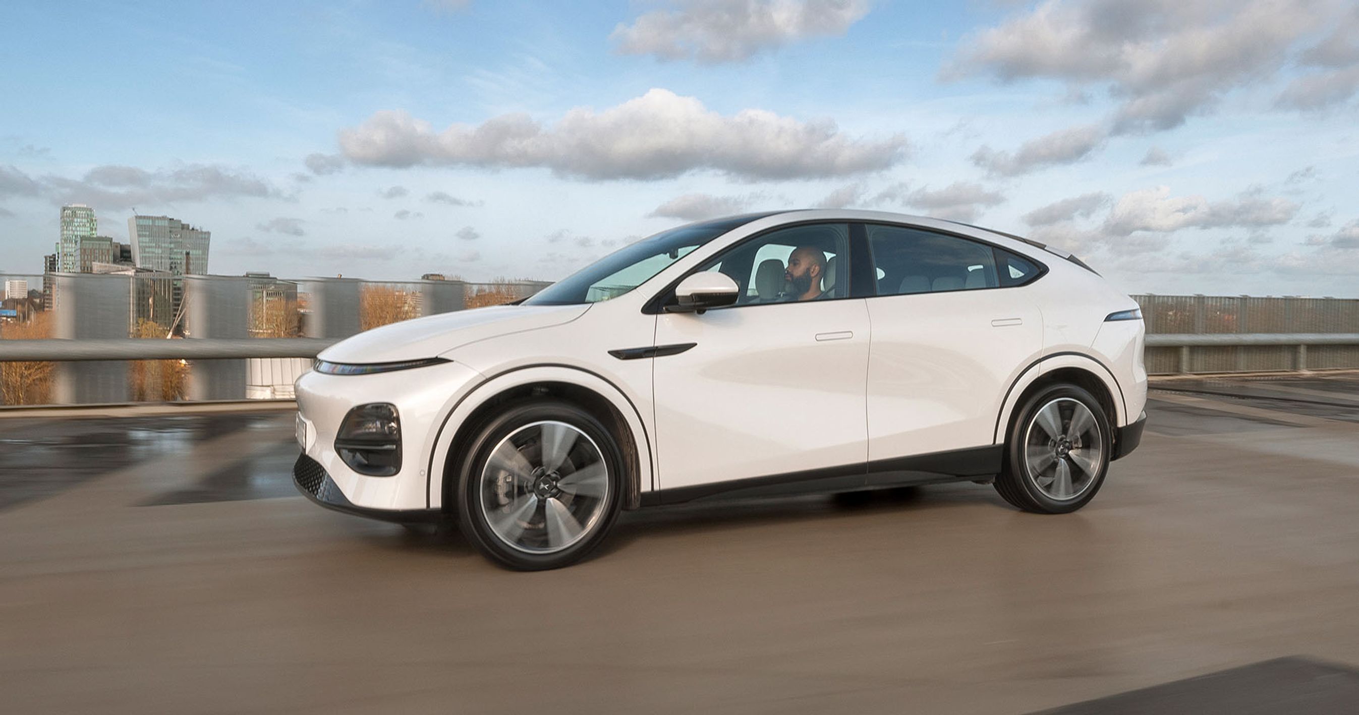 En hvid Xpeng G6 med himmel og by i baggrunden