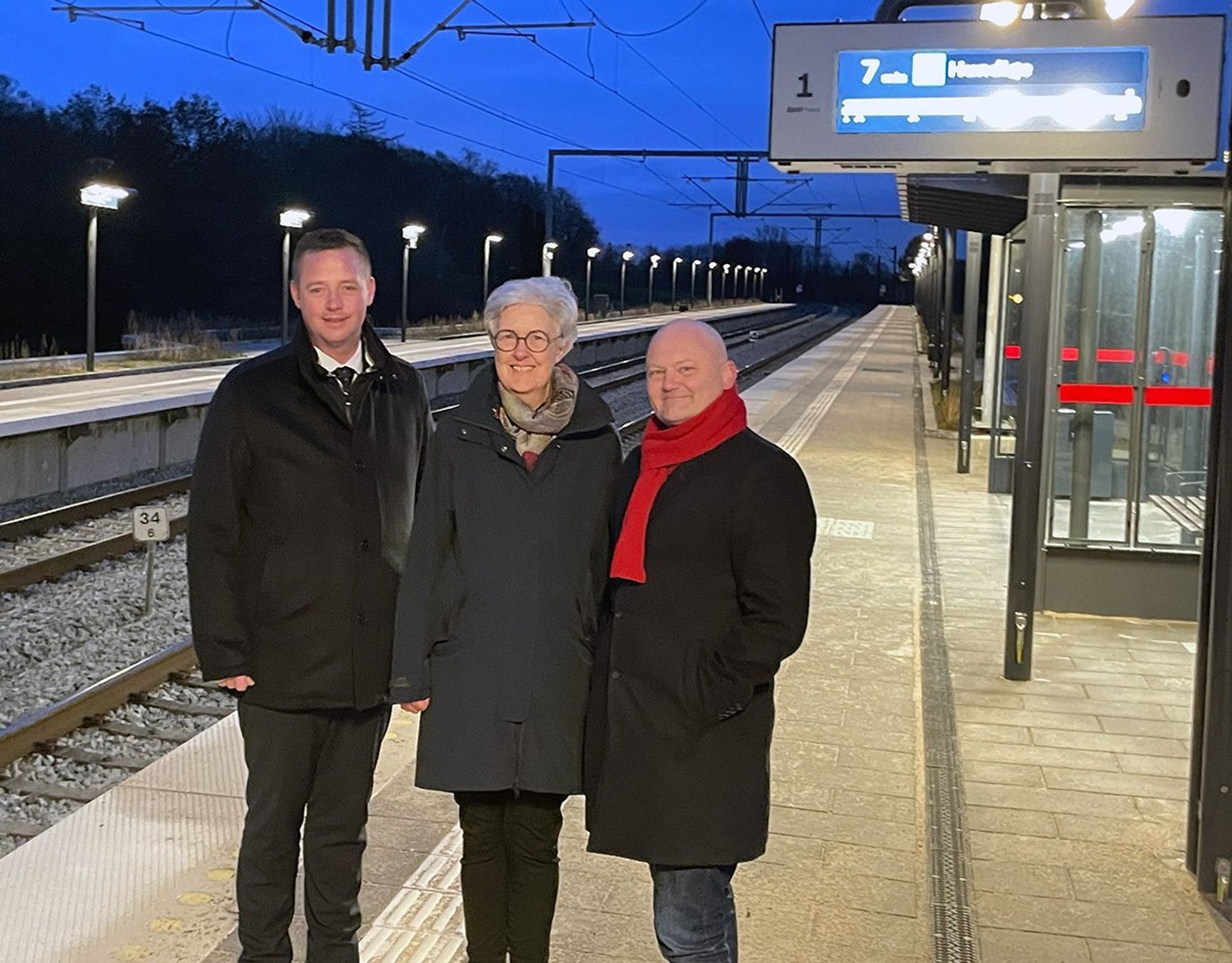 Tre personer på togperron i mørke.