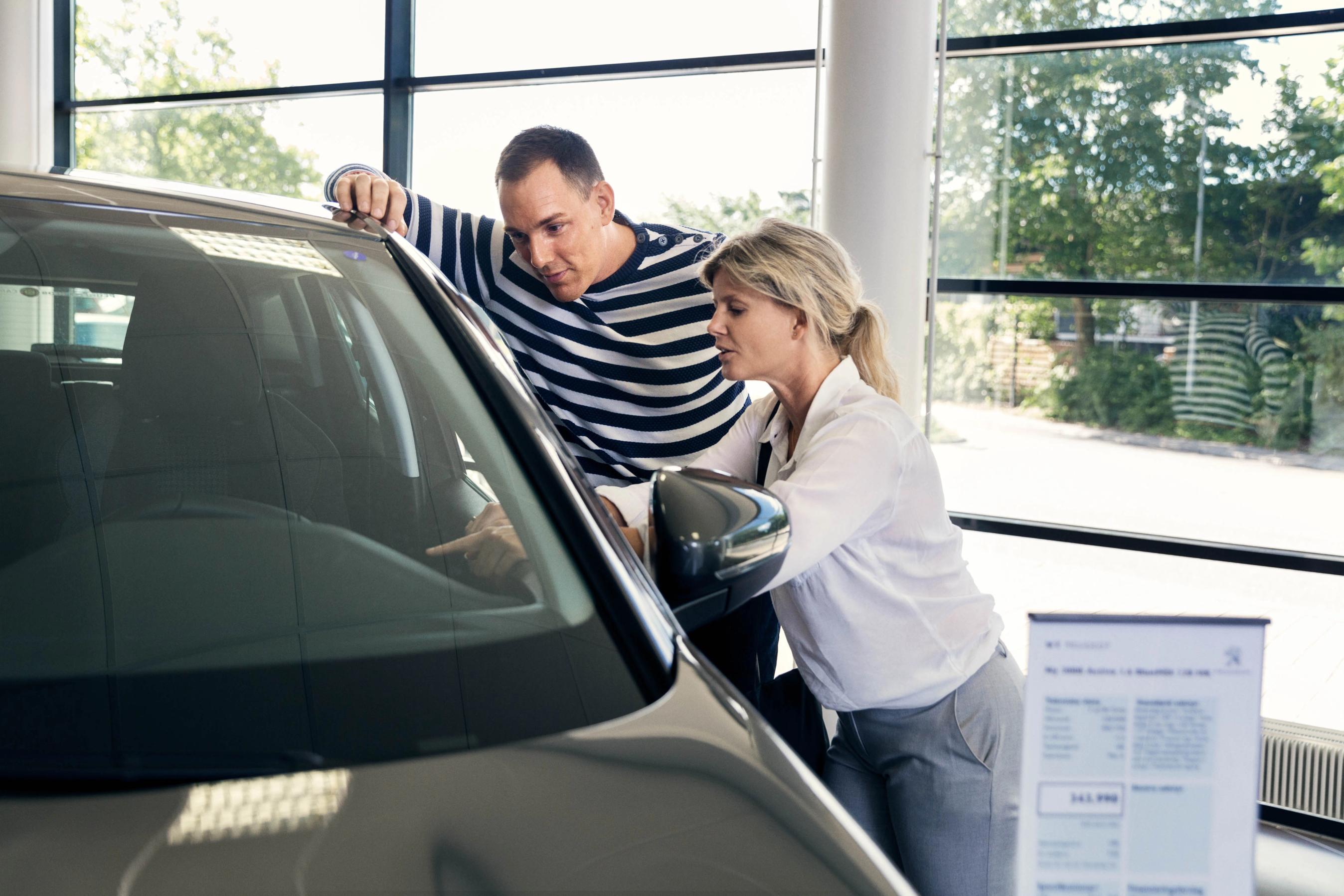 En mand og en kvinde kigger på bil hos en bilforhandler. 