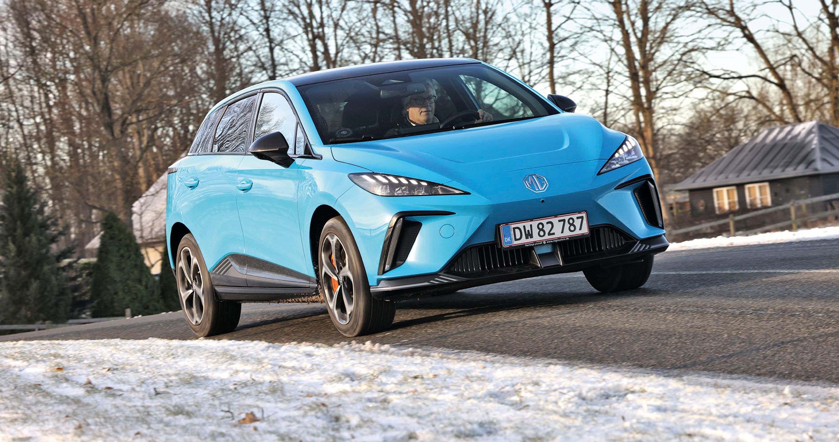 En MG 4 XPower kører i et sving med sne i forgrunden og et hus i baggrunden