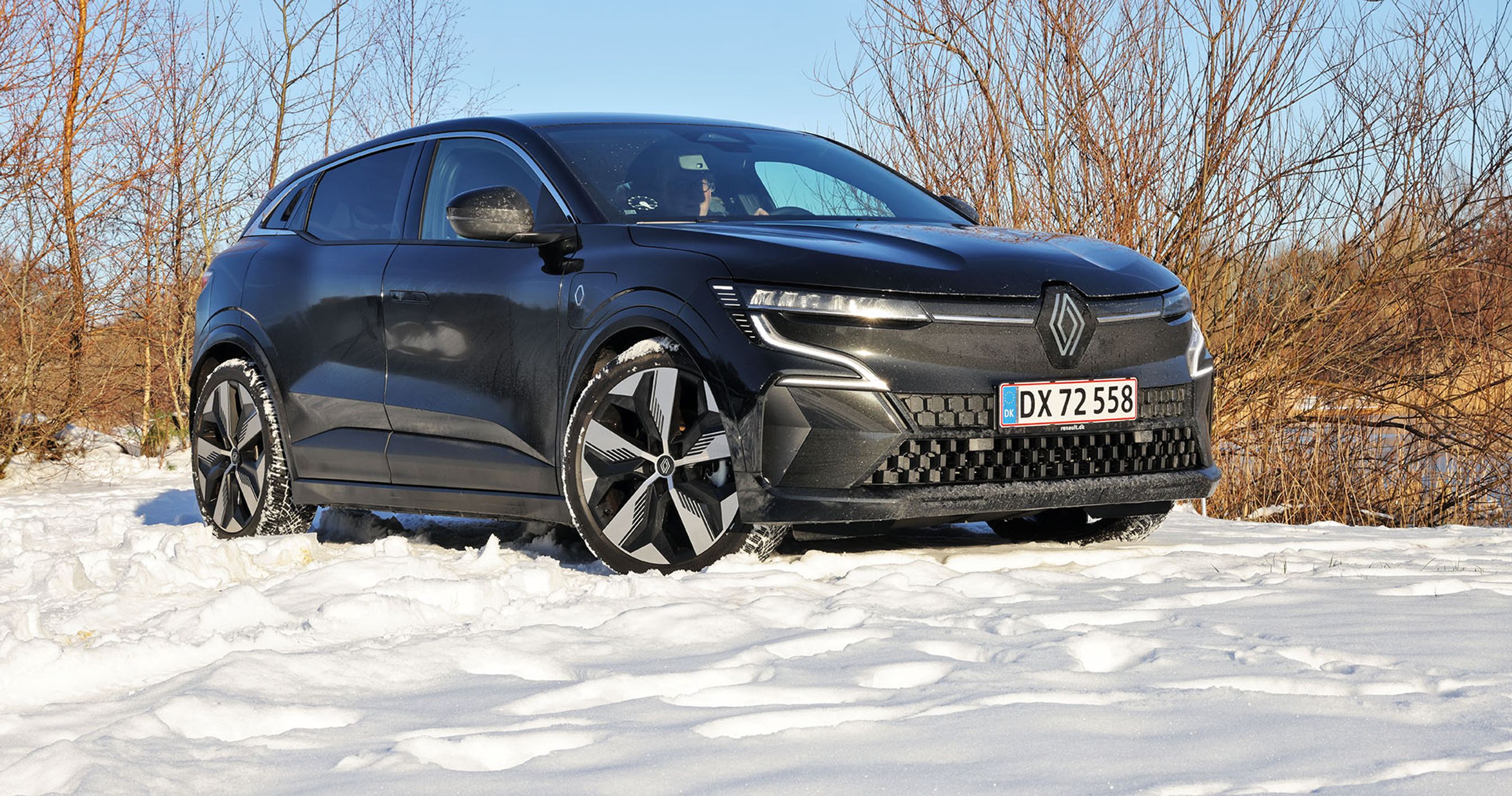 En sort Renault Megane holder i sne med buske i baggrunden