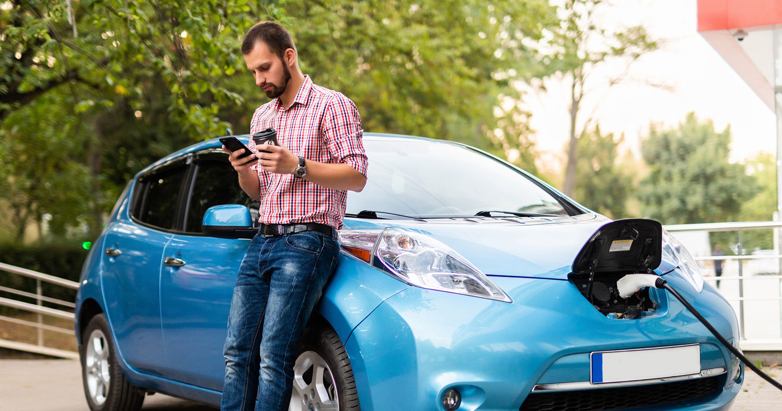 Mand ved elbil kigger på mobiltelefon