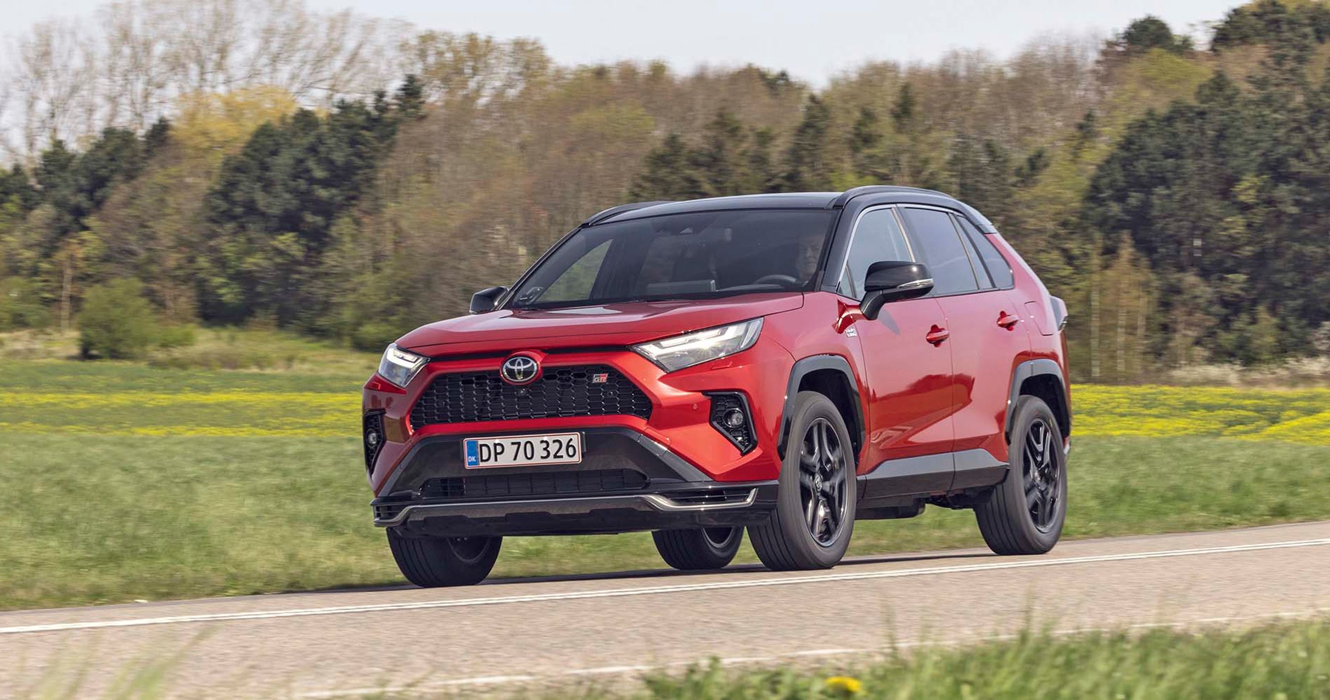 En rød Toyota RAV4 kører på en landevej med træer i baggrunden