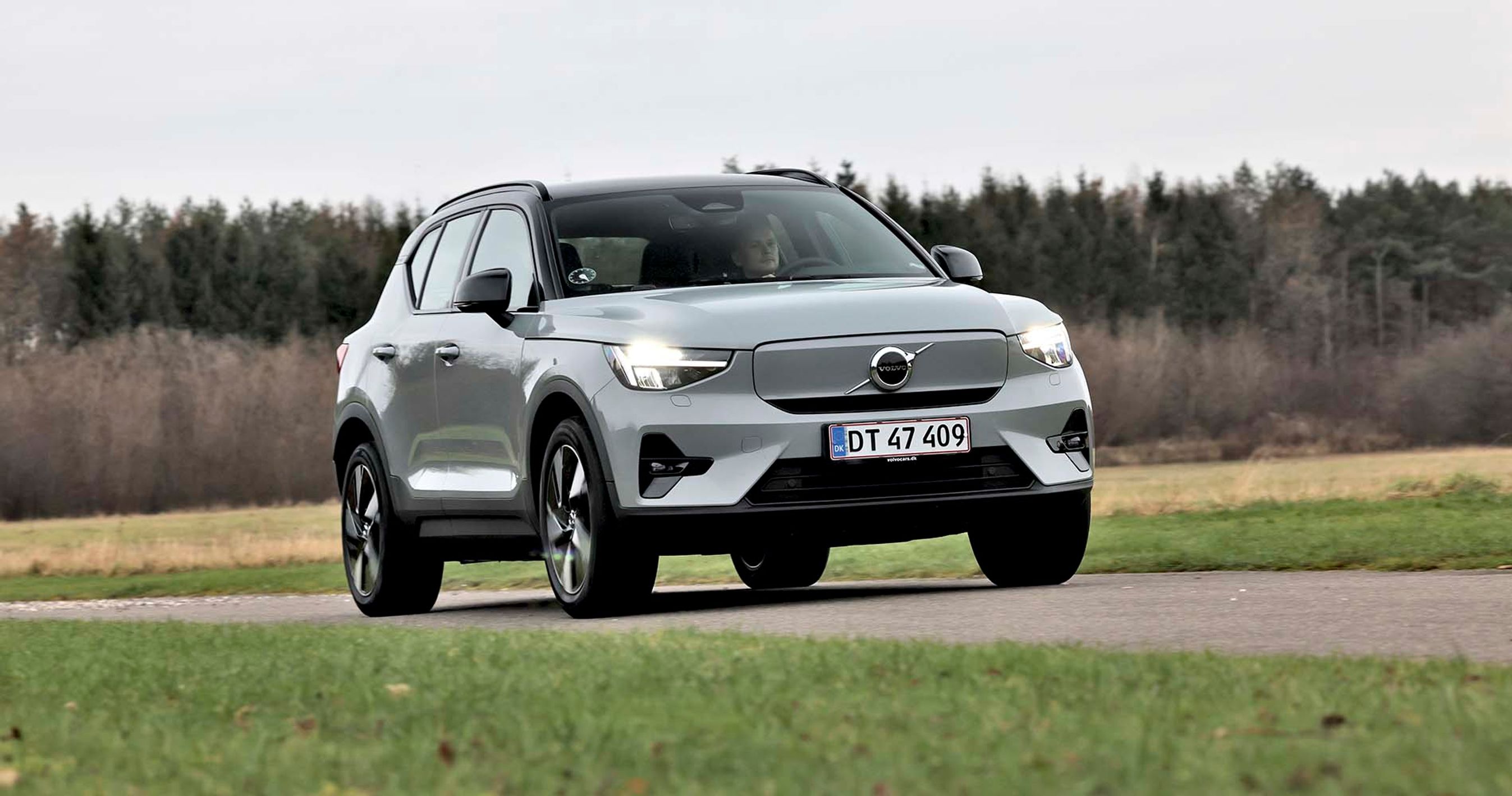 En grå Volvvo XC40 elbil kører på en landevej med græs og træer i baggrunden