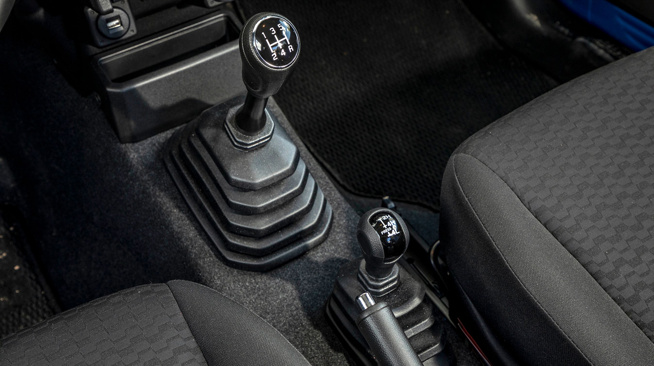 Det er sjældent set, men der er to gearstænger i Suzuki Jimny. Den store styrer gearkassens fem fremadgående gear og bakgearet, mens man med den lille vælger, om bilen skal køre med baghjulstræk (2H), firehjulstræk i høj fart (4H) eller med firehjulstræk og reduktionsgear til lav fart (4L). Med firehjulstræk kan bilen kun køre på løst underlag.