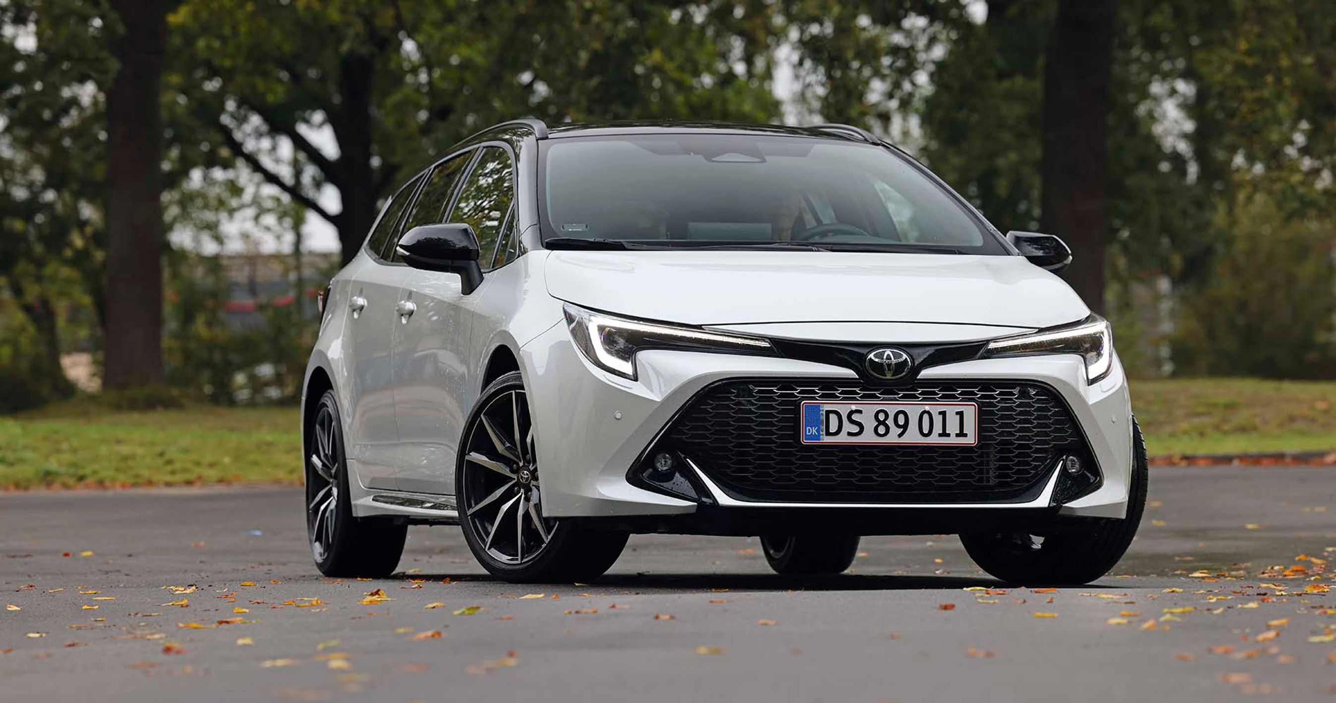 En hvid Toyota Corolla set forfra, mens den holder foran træer