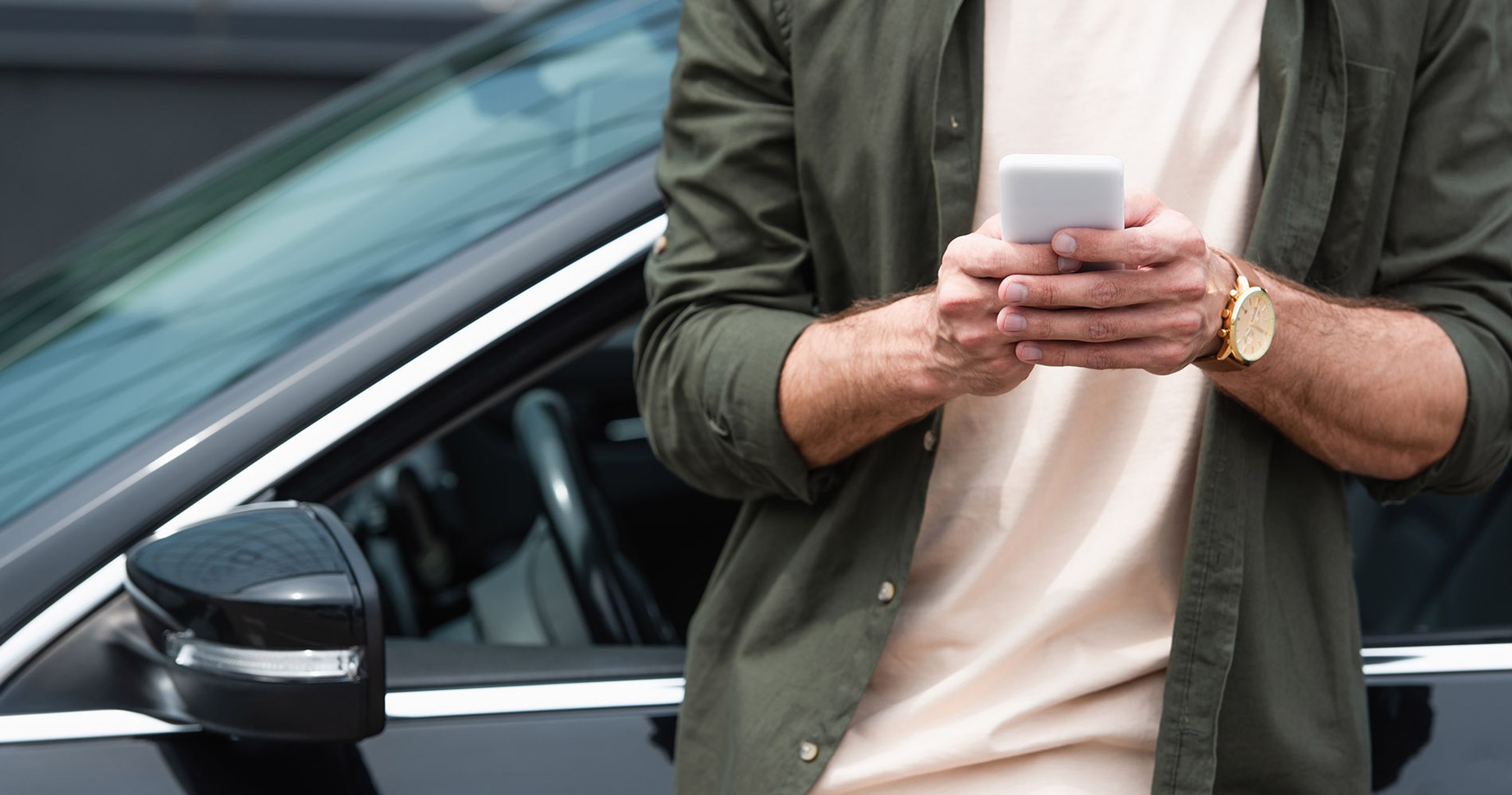 Mand står foran bil og kigger på sin mobil.