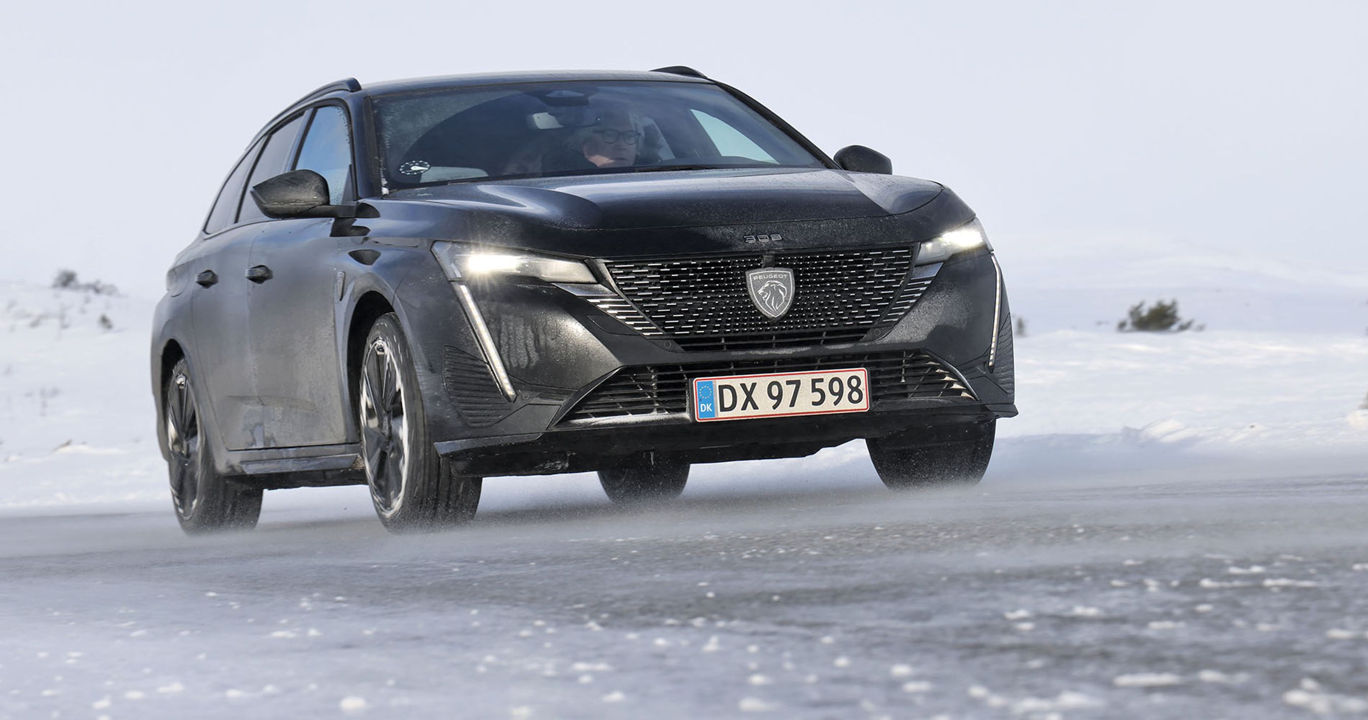 En mørk Peugeot E-308 set forfra kører på en snedækket vej