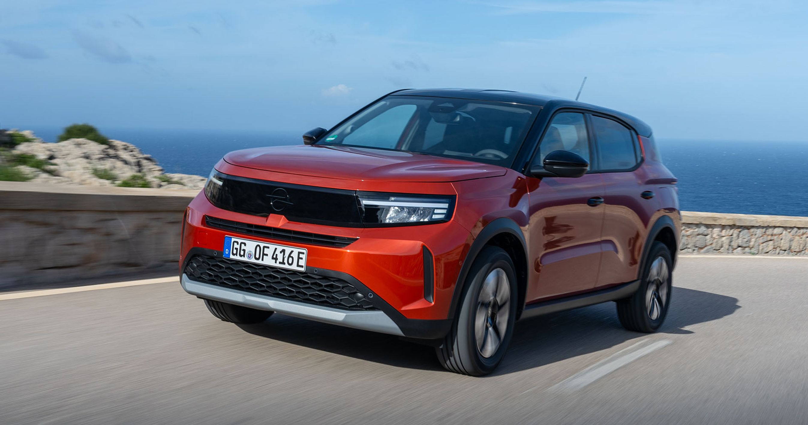 Rød Opel Frontera kører i sving på bjergvej med havet i baggrunden