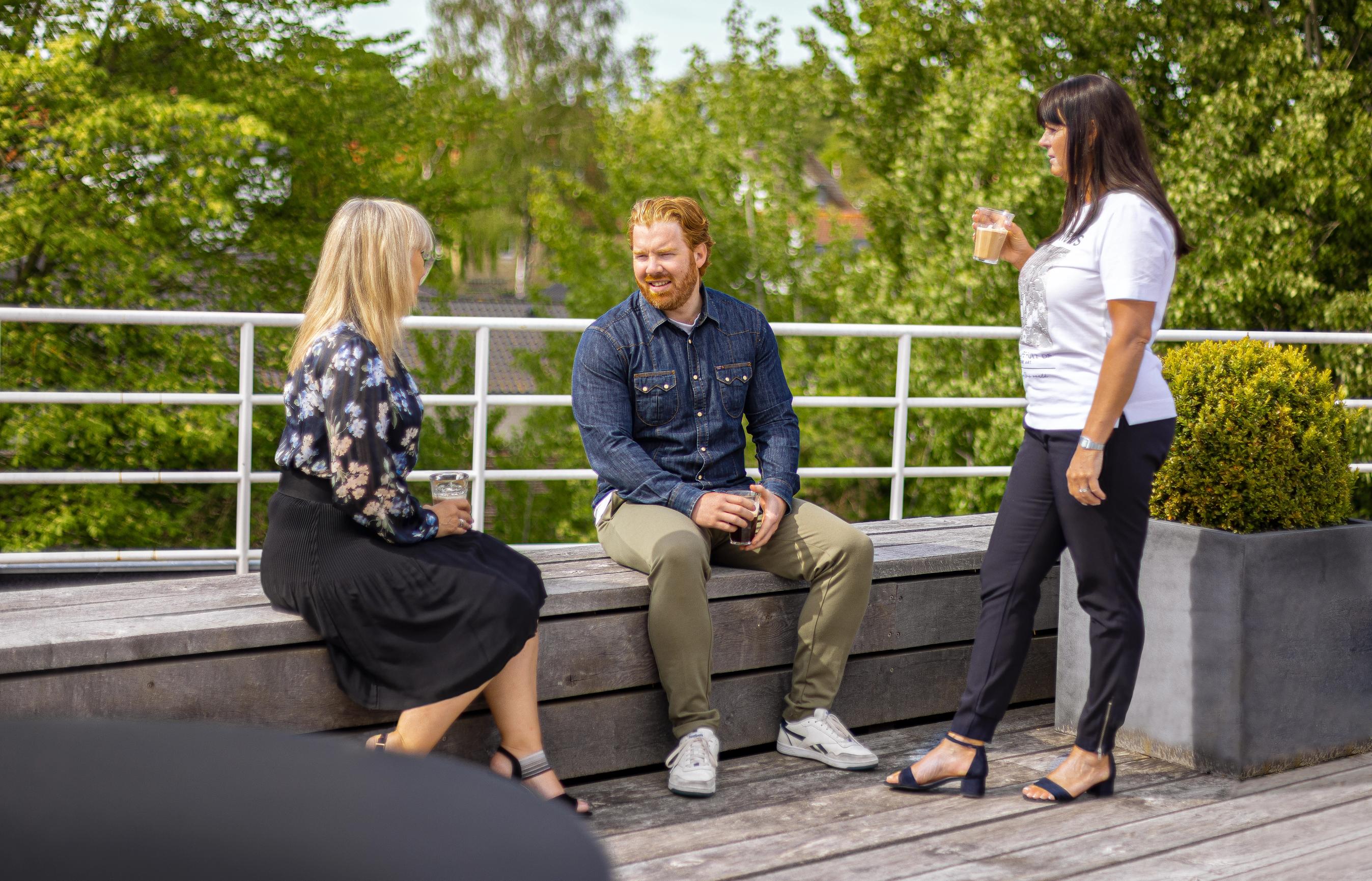 Tre personer drikker kaffe på en terrasse