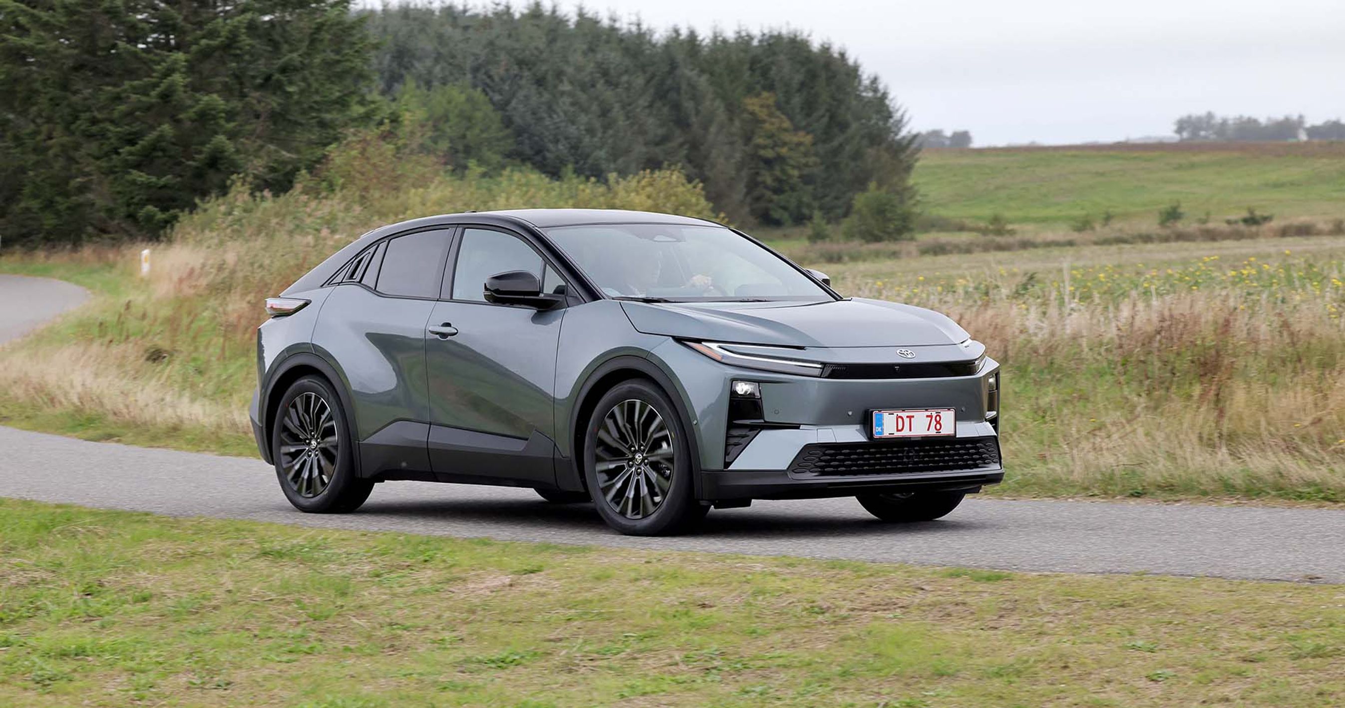 Toyota C-HR+ kører på landevej med træer og marker i baggrunden