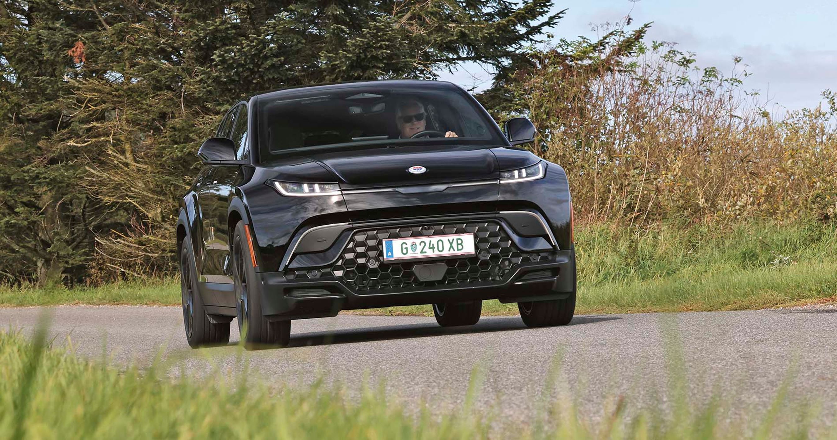 Elbilen Fisker Ocean set forfra, mens den kører på en landevej med træer i baggrunden.