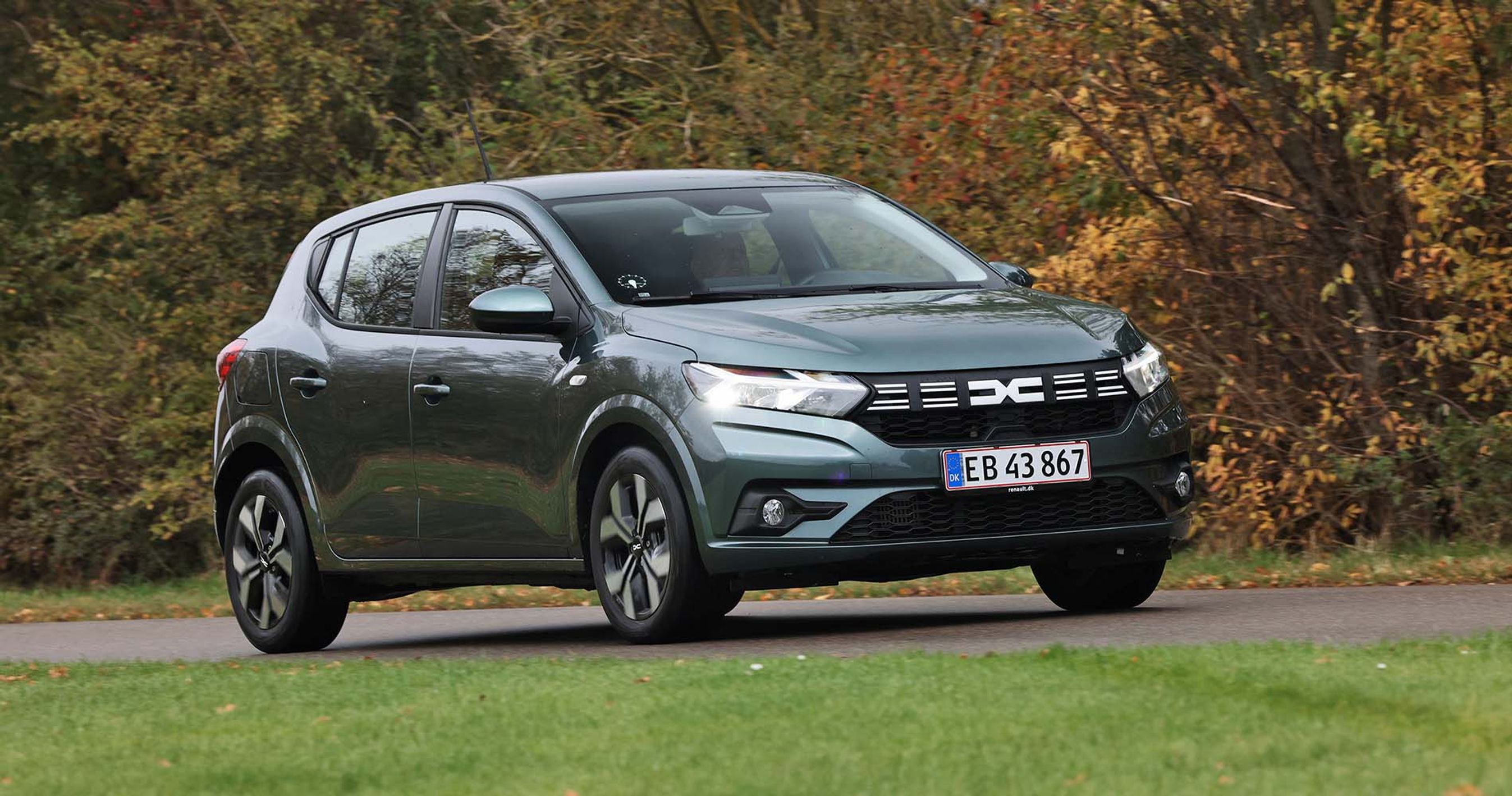 Dacia Sandero kører på landevej med træer i efterårsfarver i baggrunden