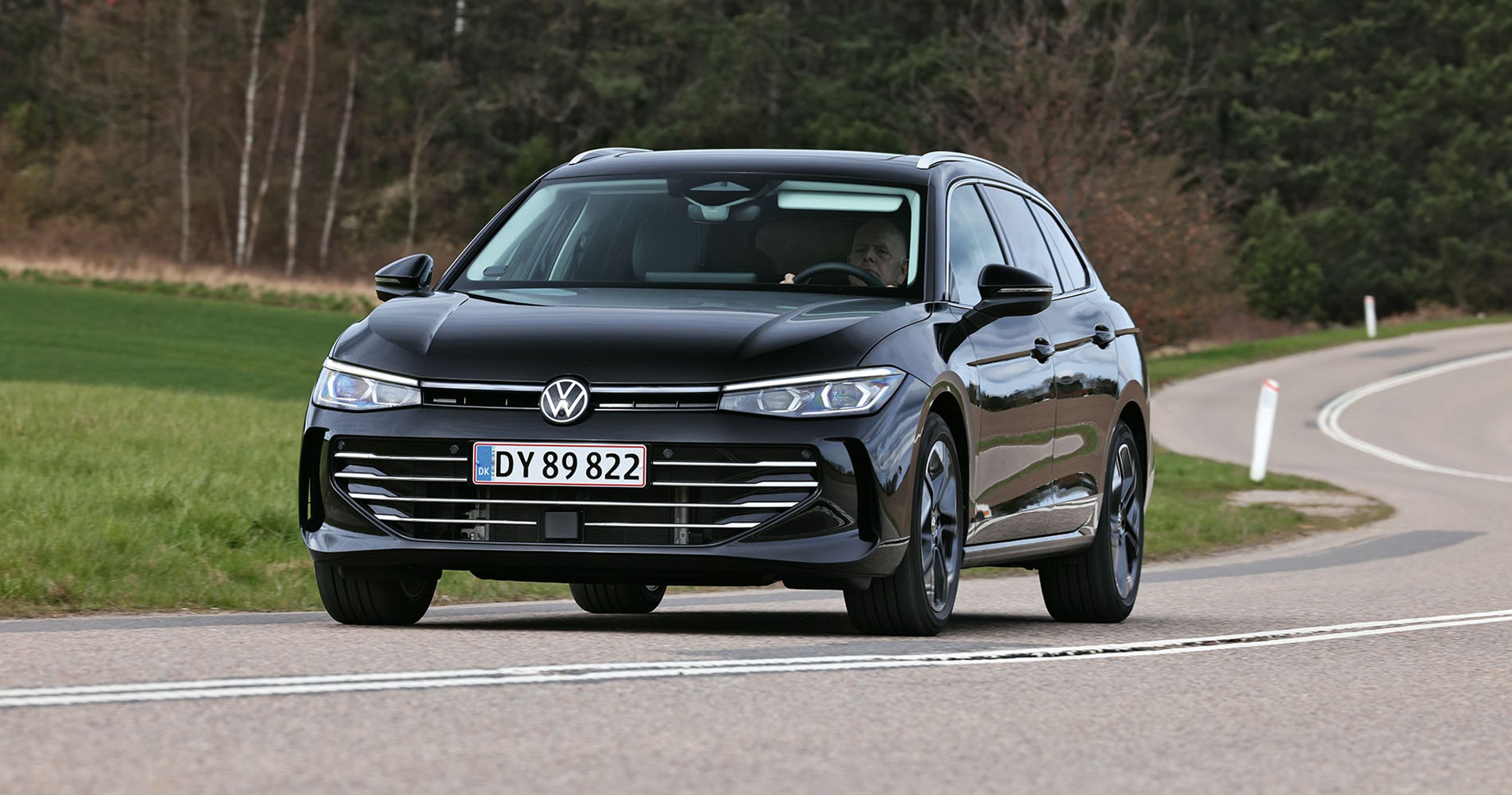En sort VW Passat kører gennem et sving med skov i baggrunden