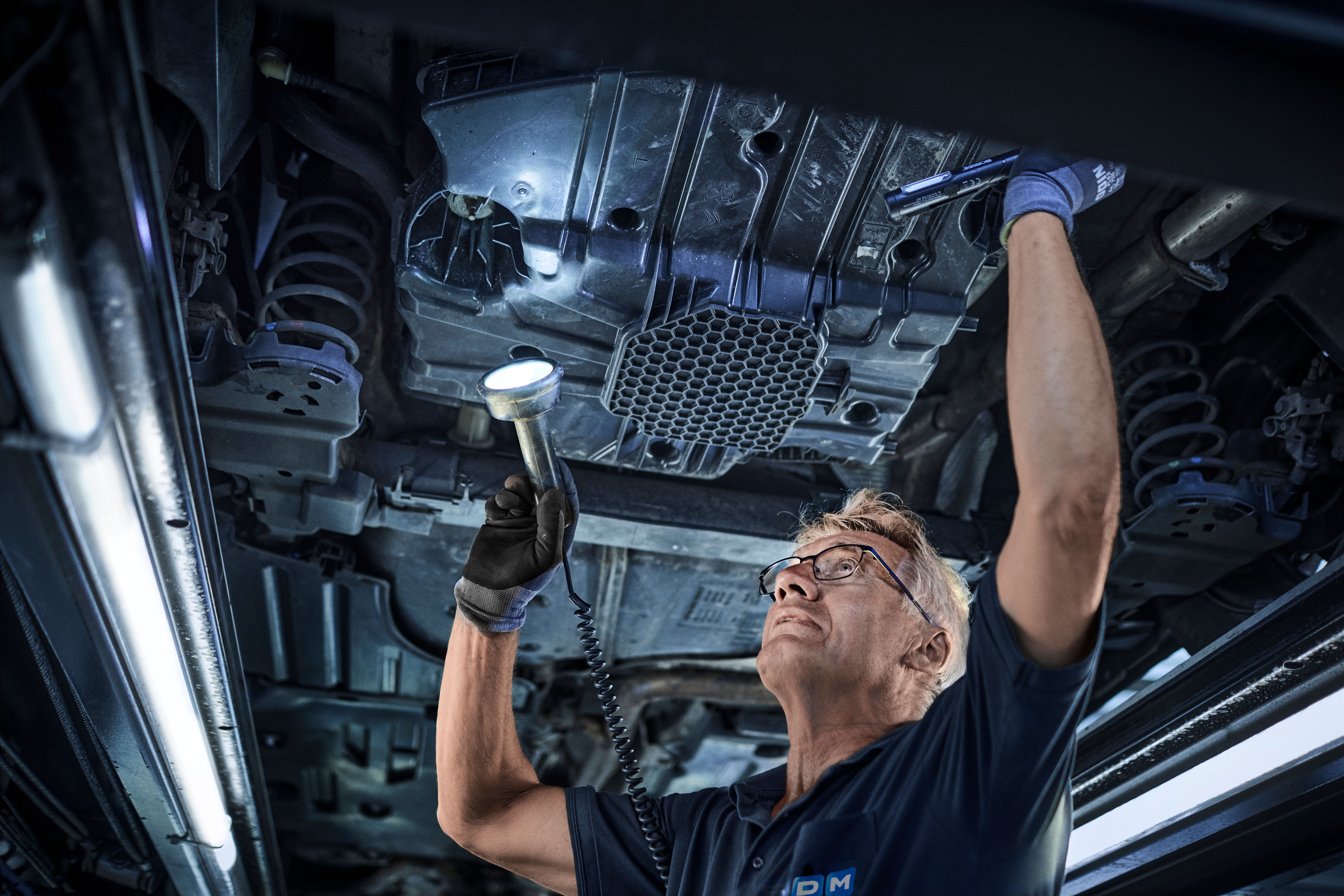 FDM medarbejder tjekker undervognen på en bil der er oppe på en lift - Test og Bilsyn