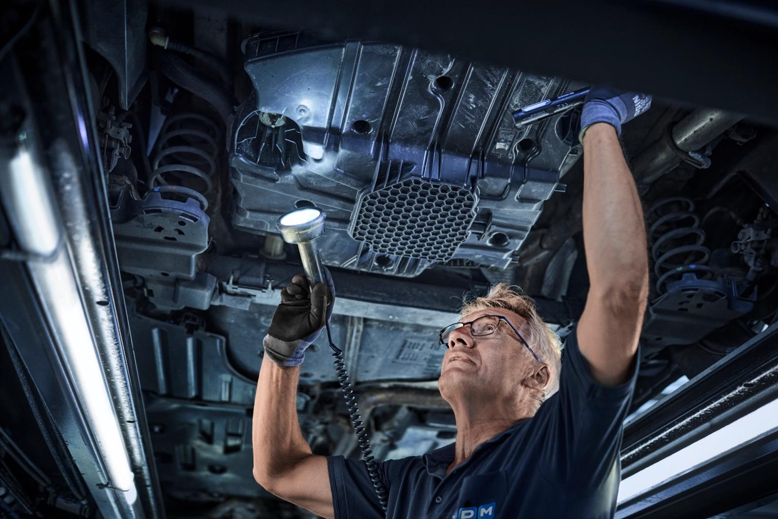 FDM medarbejder tjekker undervognen på en bil der er oppe på en lift