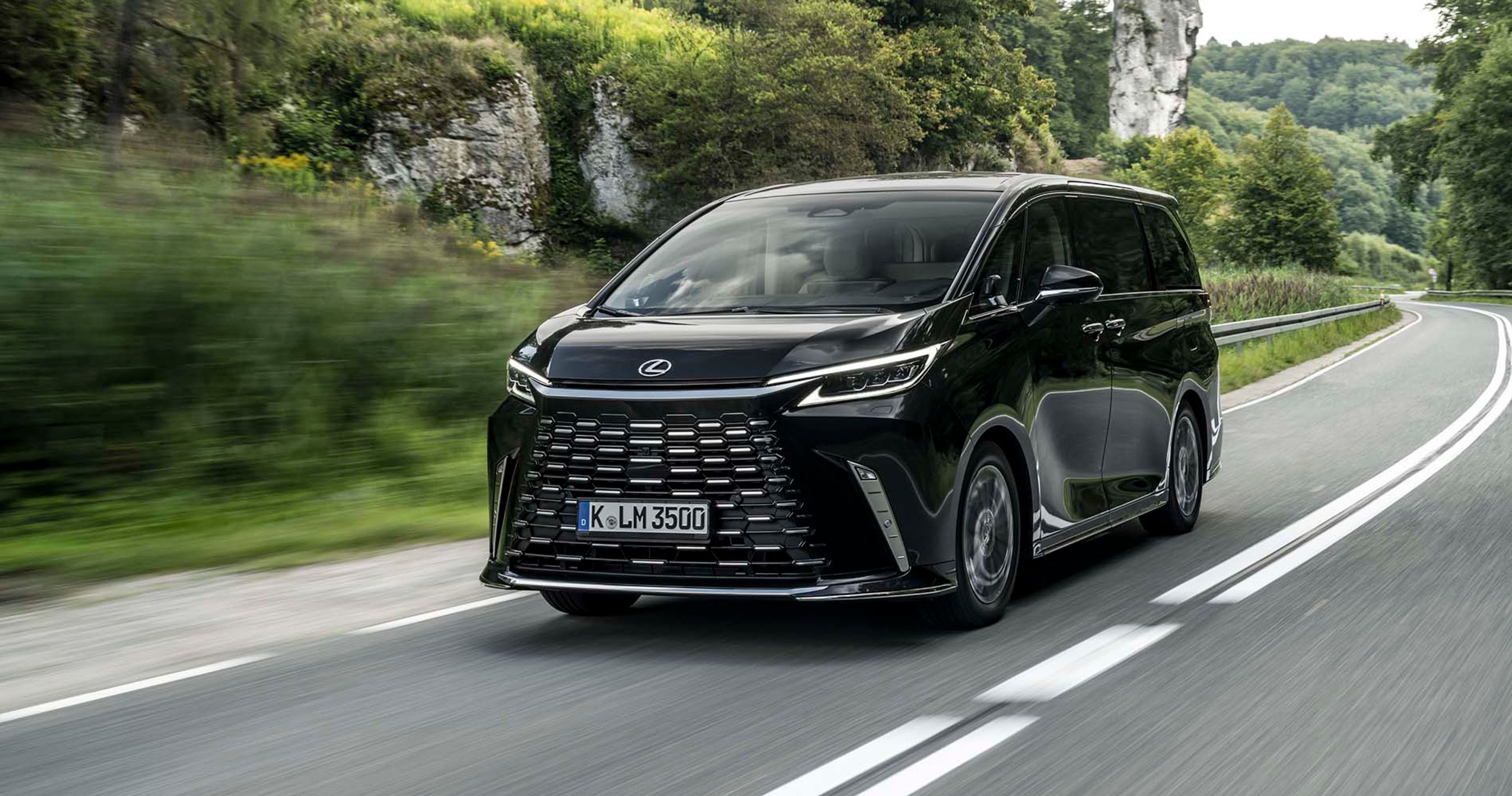 Luksus-minibussen Lexus LM kører på en landevej med klipper i baggrunden