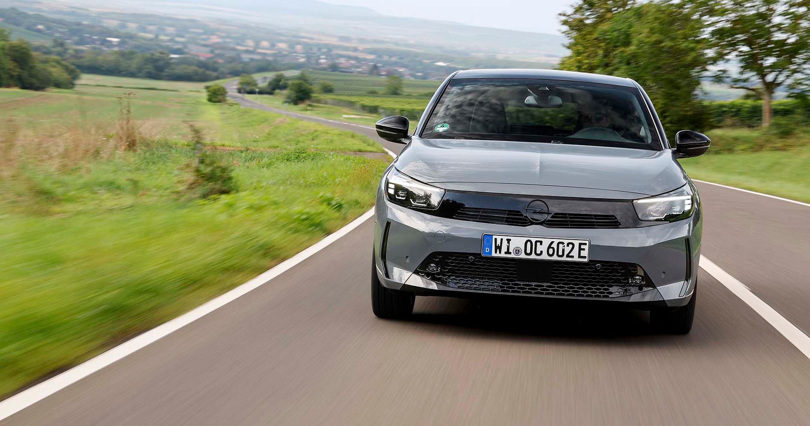 En grå Opel Corsa set forfra kører på en landevej.