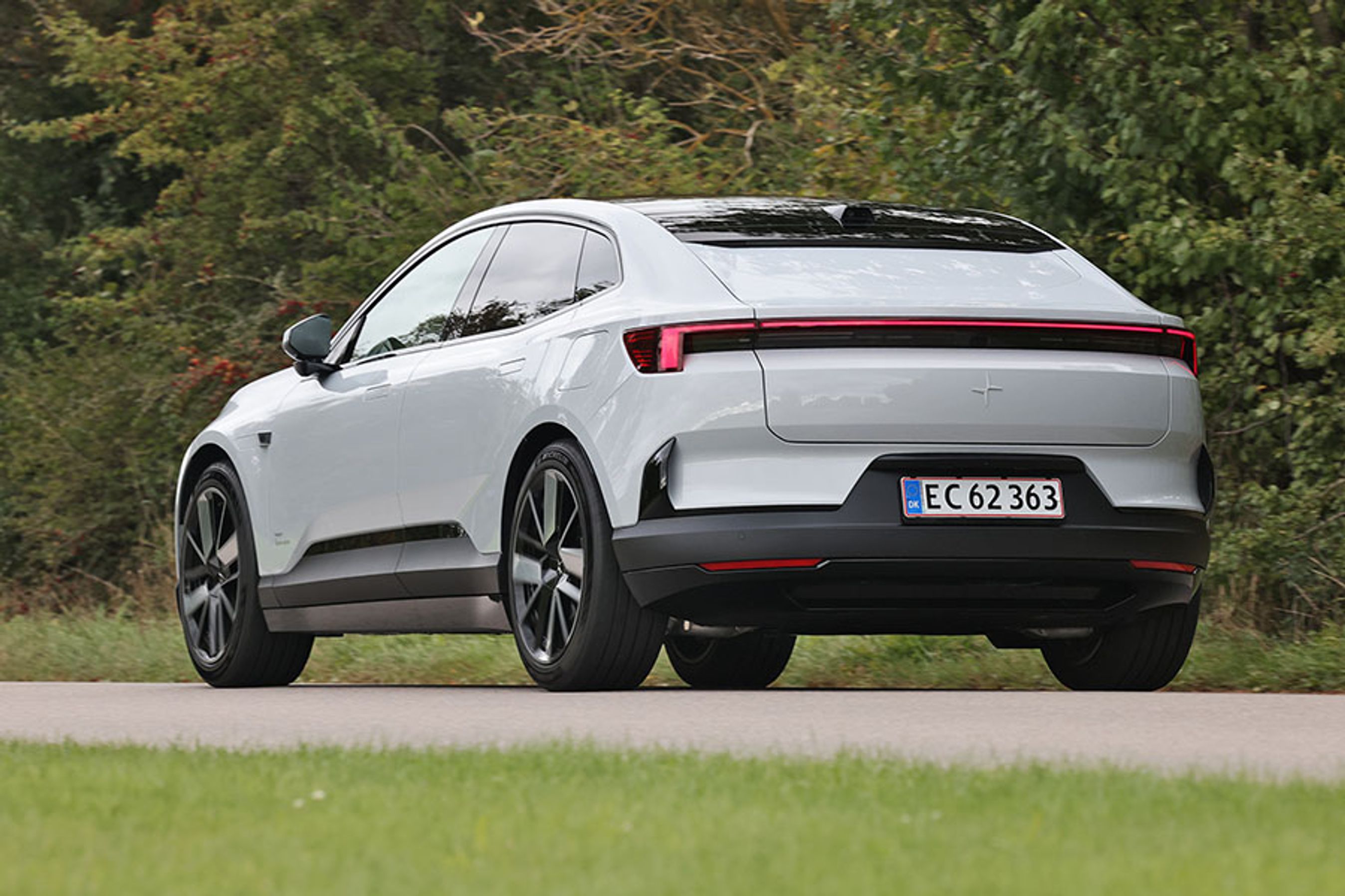 En Polestar 4 set bagfra kører på en vej med træer i baggrunden.