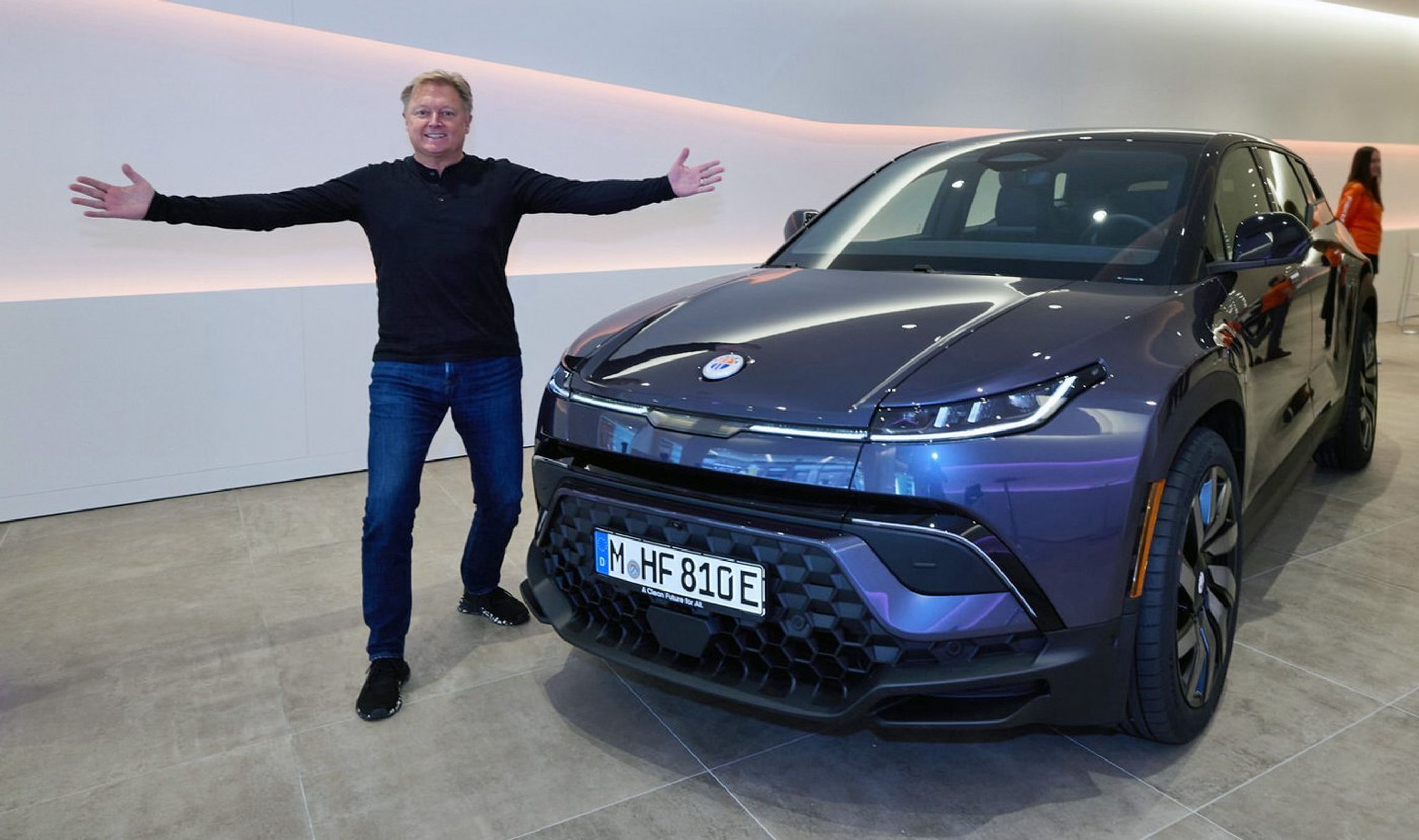 Henrik Fisker slår ud med armene foran blå bil.