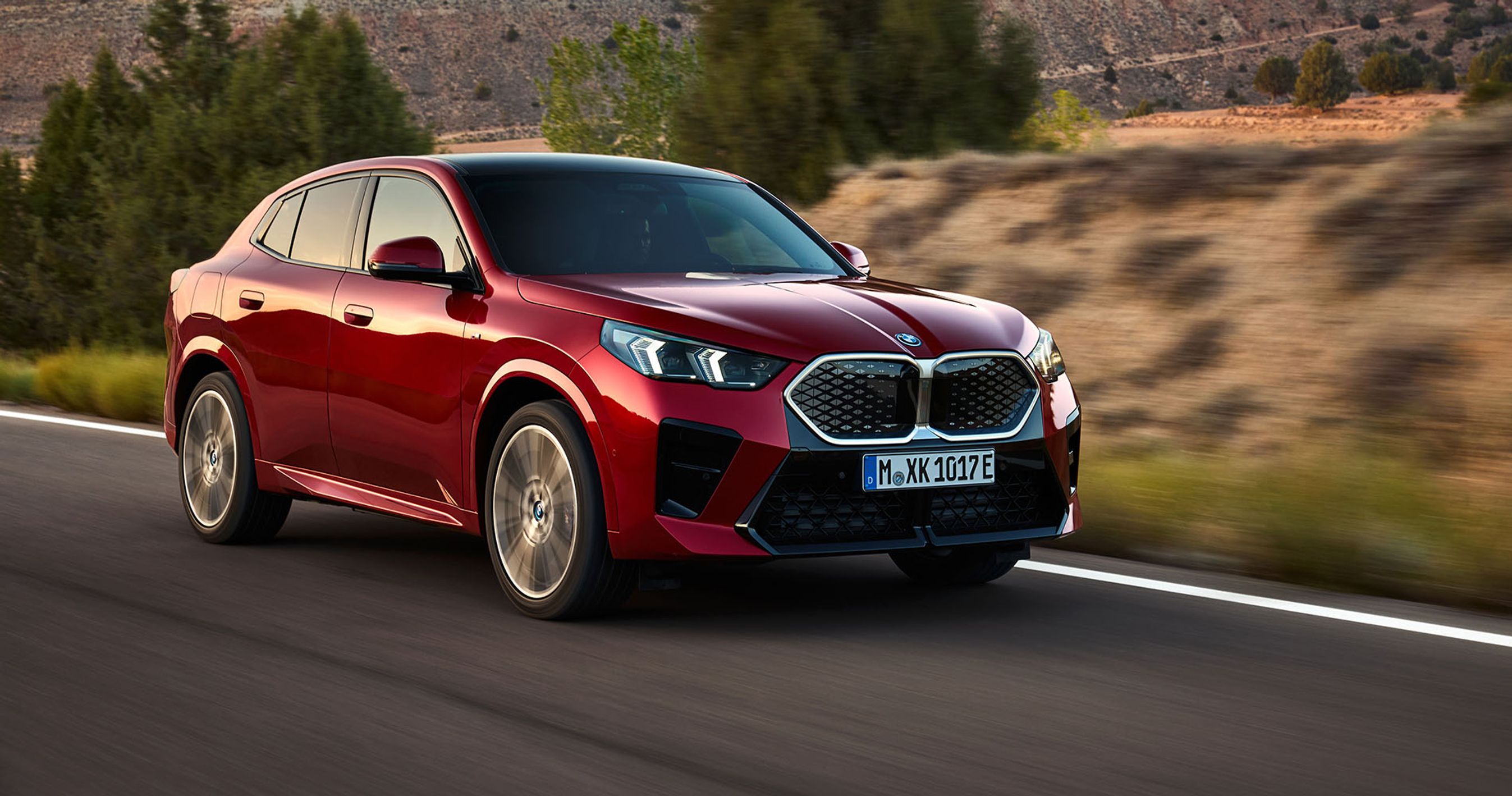 En rød BMW iX2 kører i solnedgangen i et landskab