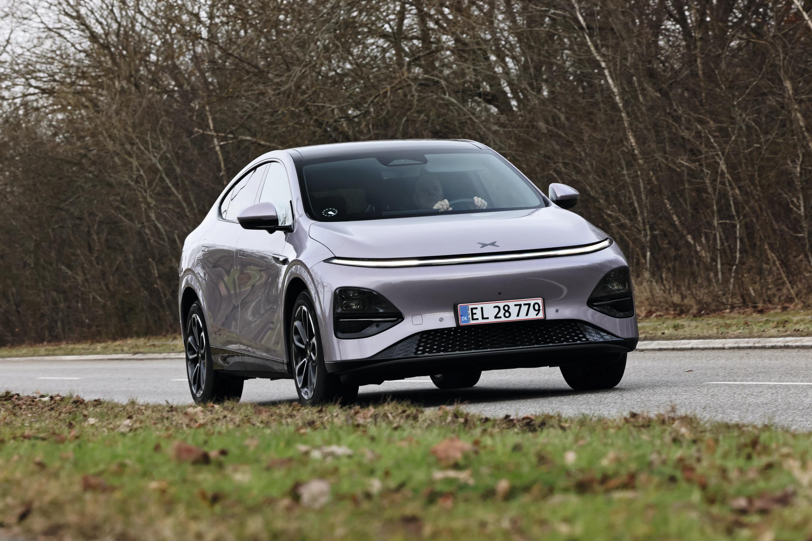 Xpeng G6 Performance set forfra, mens den kører på vej. Der er græs i forgrunden og træer i baggrunden