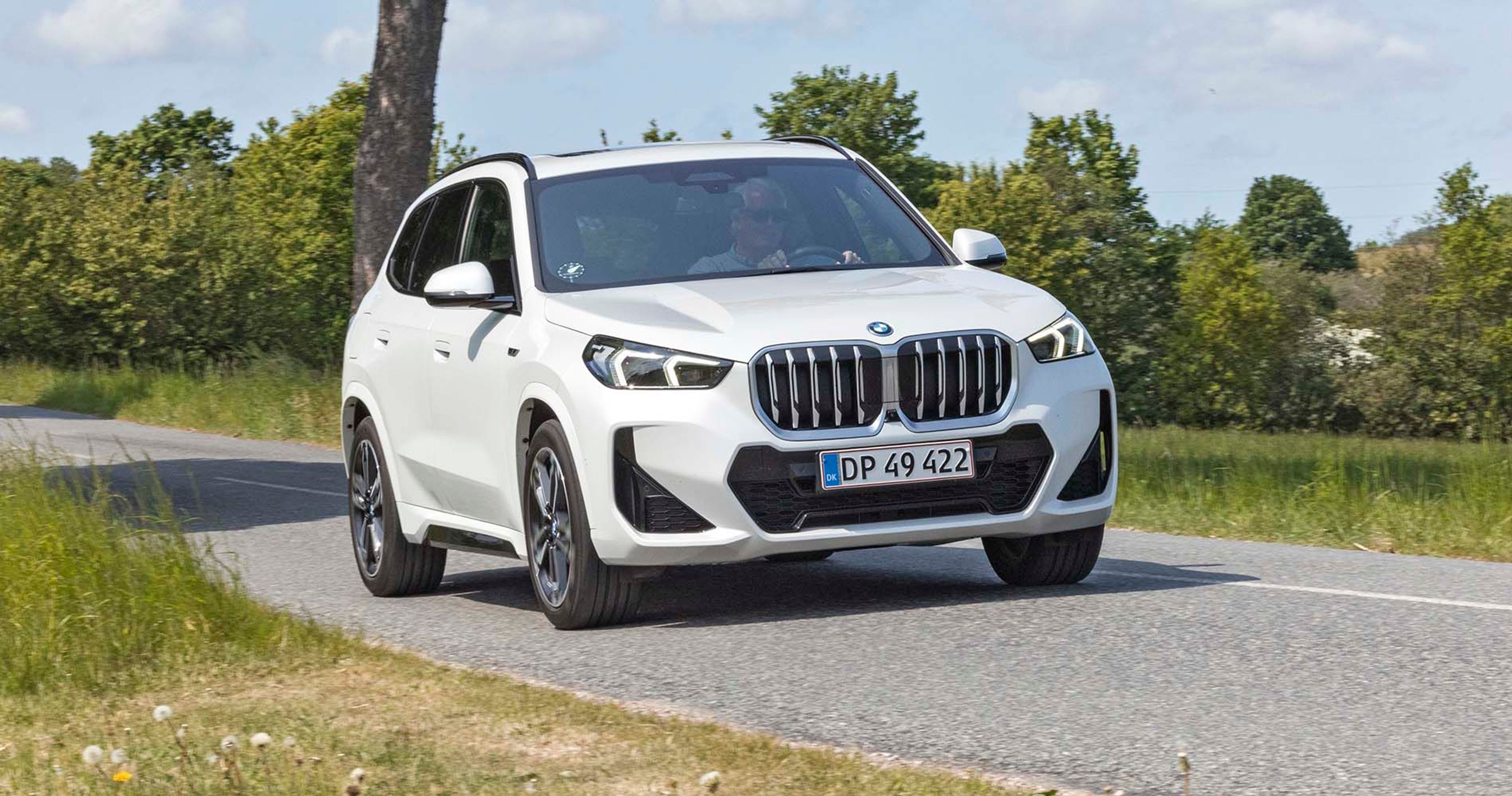 En hvis BMW X1 kører på en landevej med træer i baggrunden