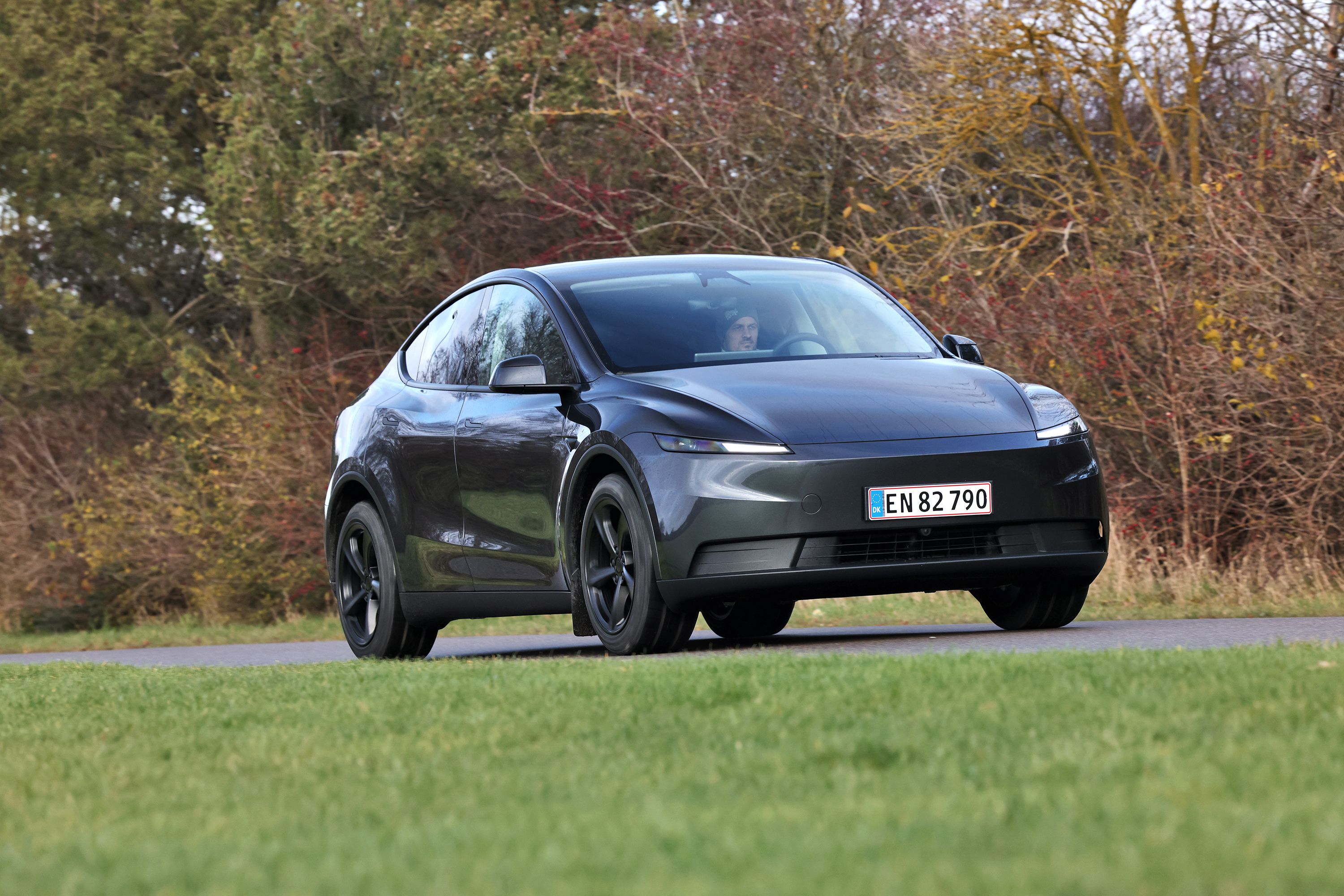 Tesla Model Y set skråt forfra, mens den kører på landevej med træer i baggrunden