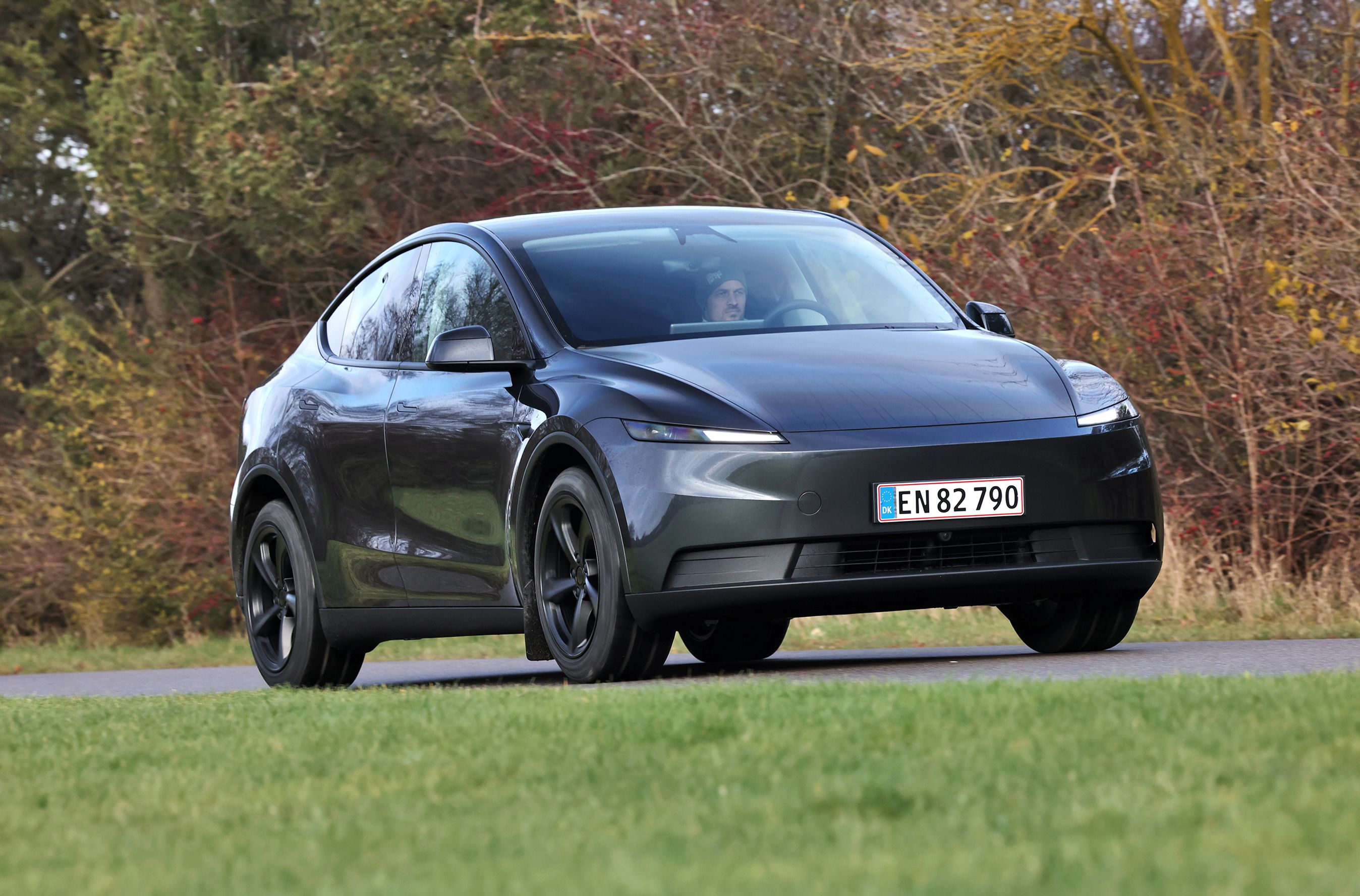 Tesla Model Y set skråt forfra, mens den kører på landevej med træer i baggrunden