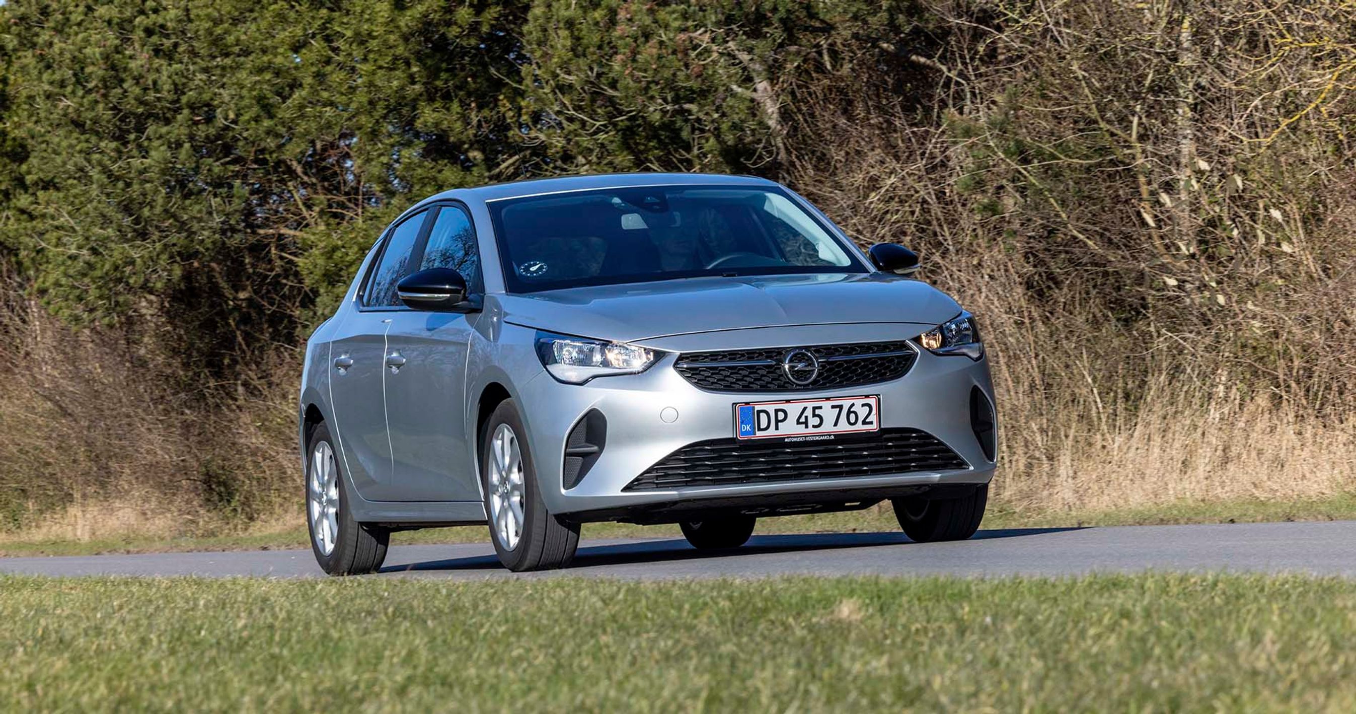 En sølvgrå Opel Corsa kører på landevej med træer i baggrunden