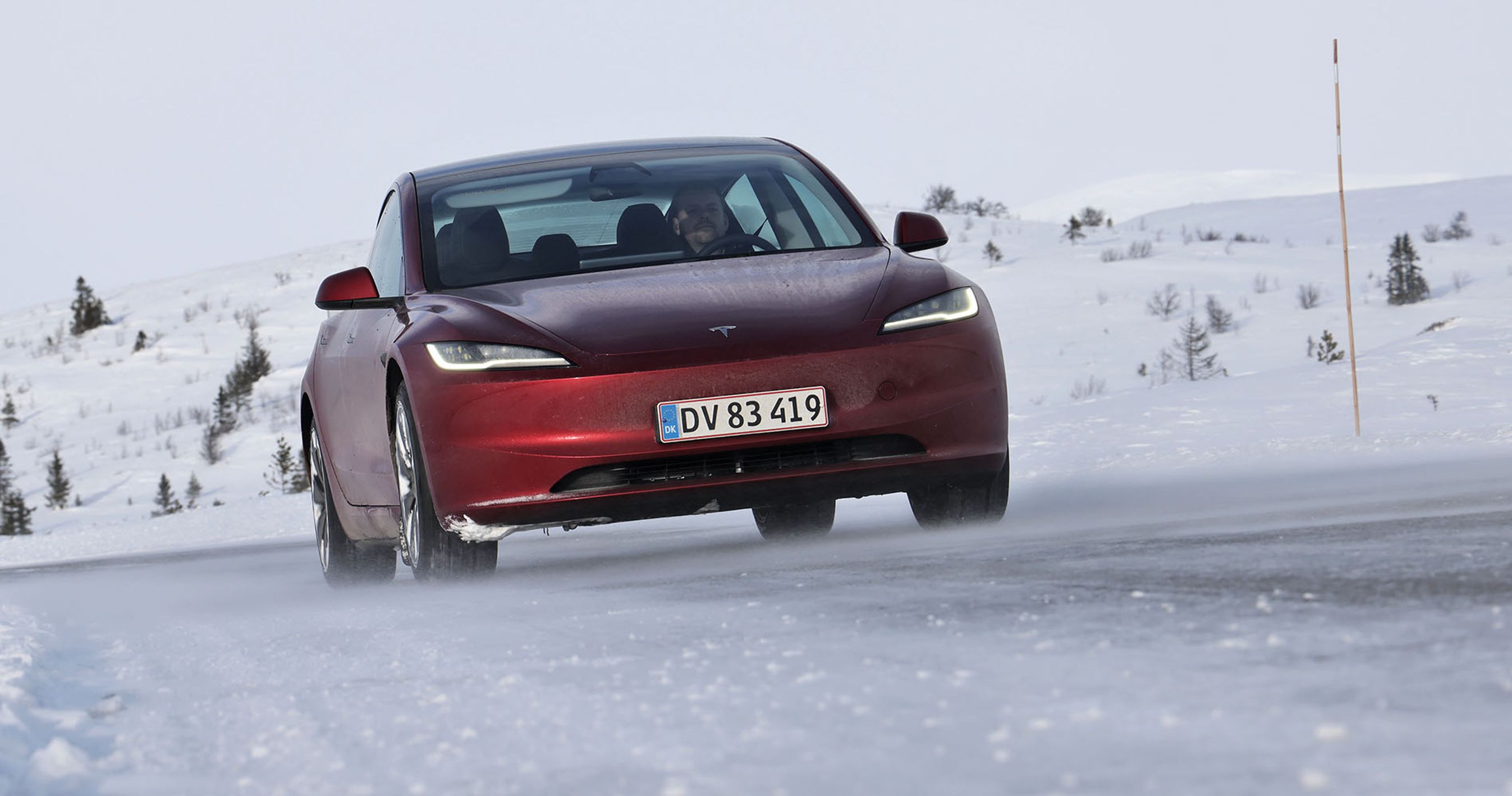 En rød Tesla Model 3 set forfra kører i snelandskab