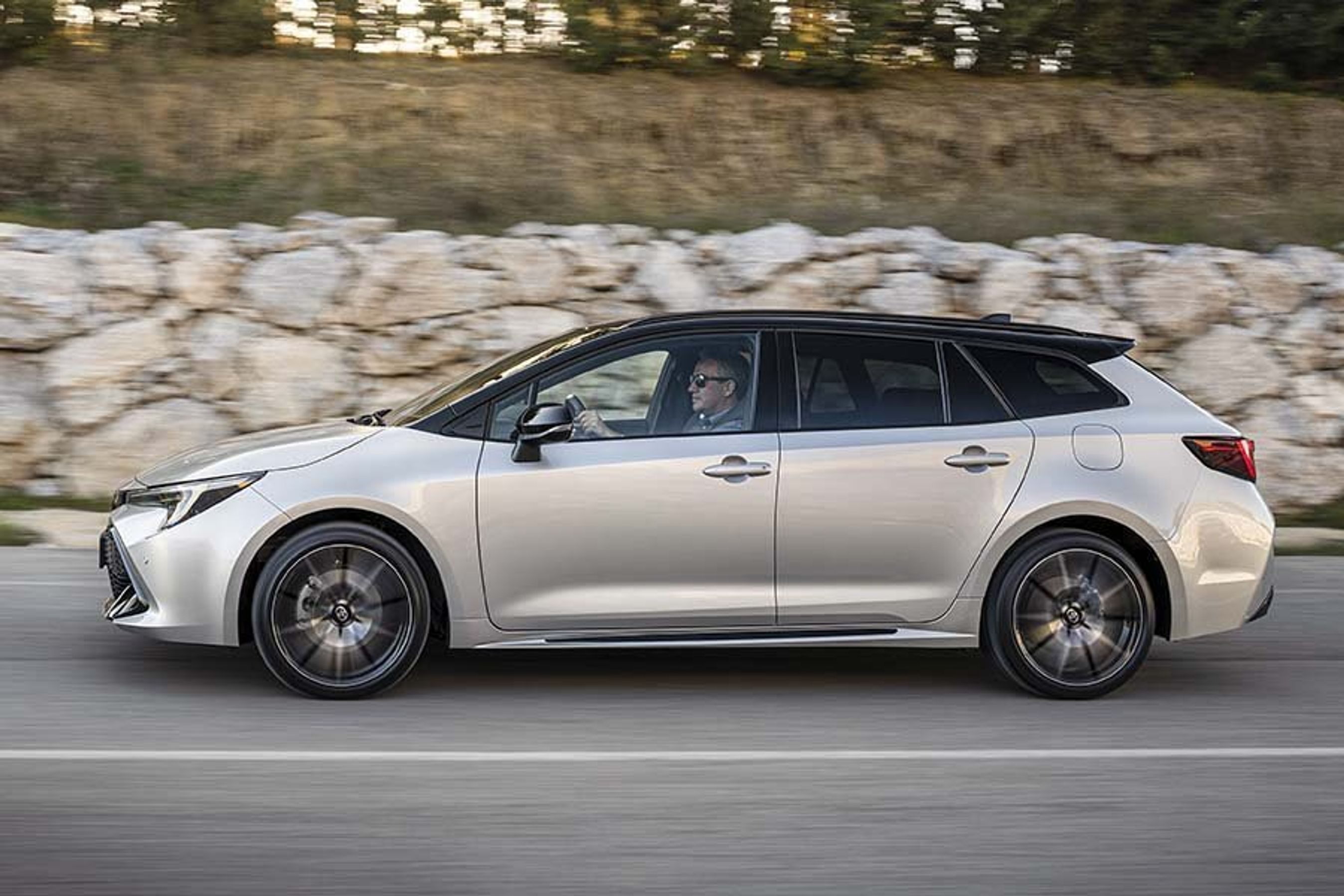 Toyota Corolla set fra siden, mens den kører på en vej med en stenvæg i baggrunden