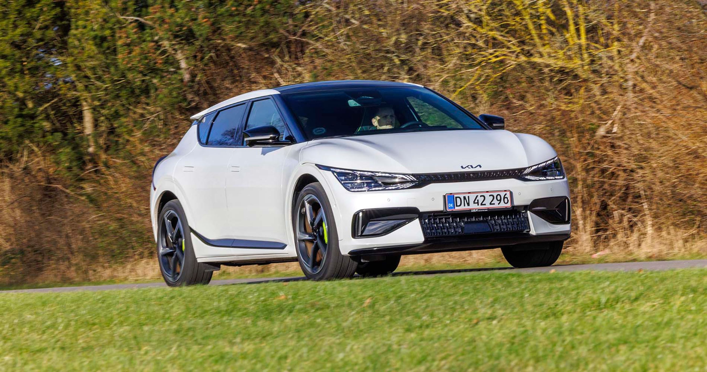 En hvid Kia EV6 GT kører på landevej med buske i baggrunden