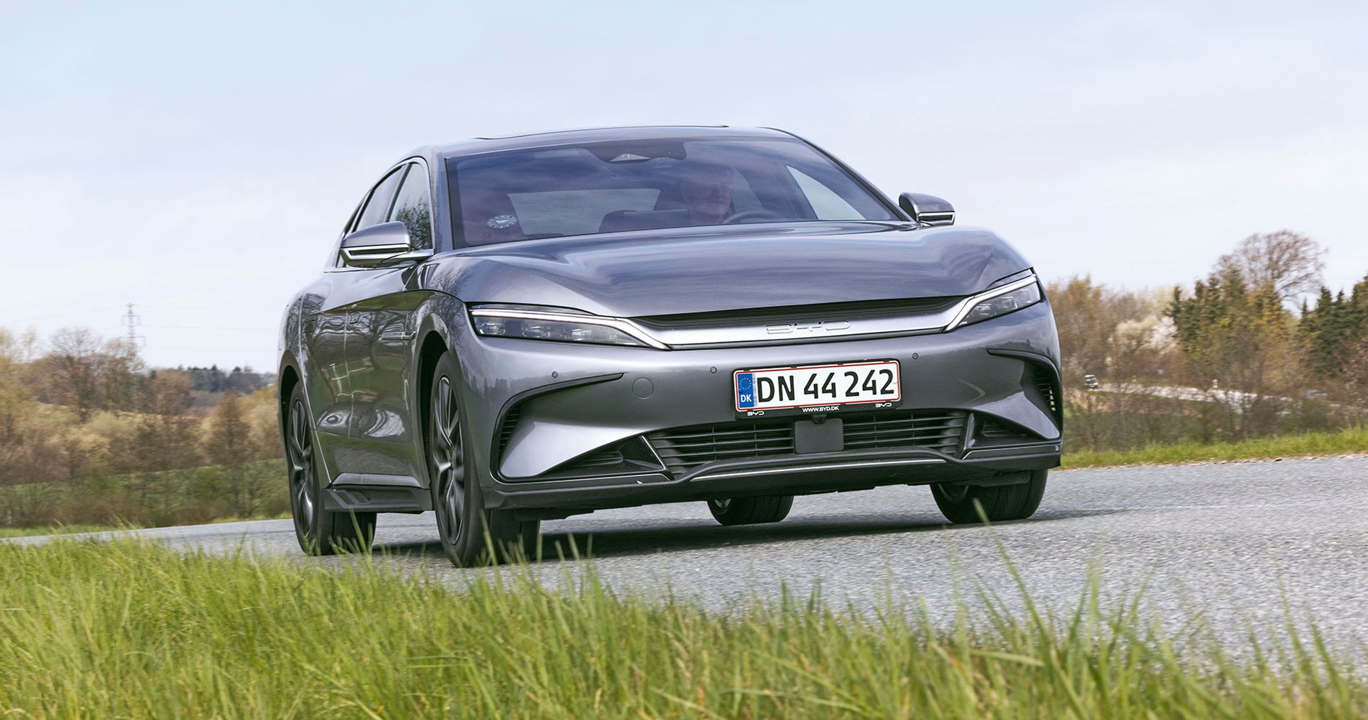Elbilen BYD Han set forfra, mens den kører på en landevej med græs i forgrunden