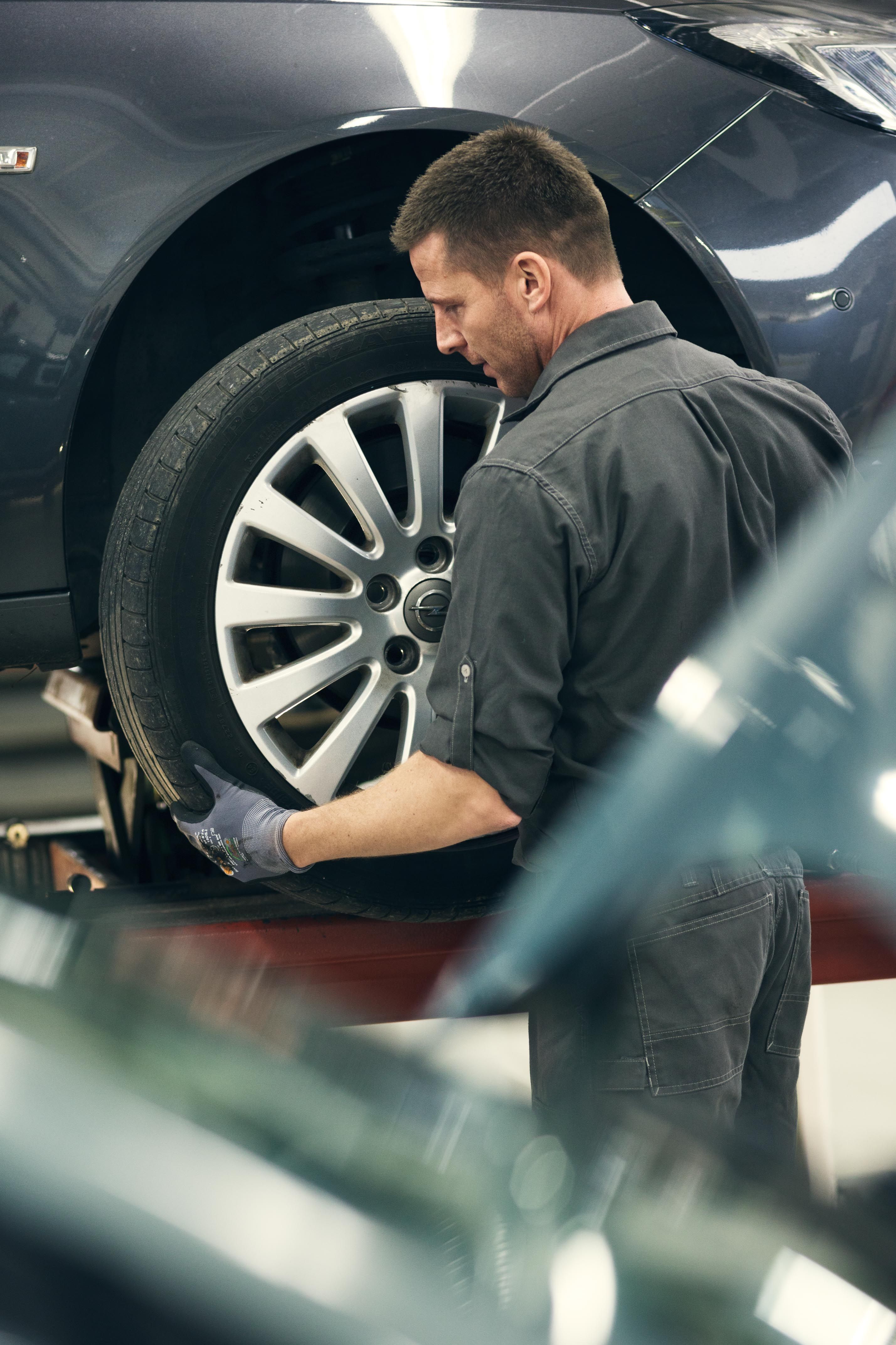 Montering af hjul på bil, der holder på værksted. 