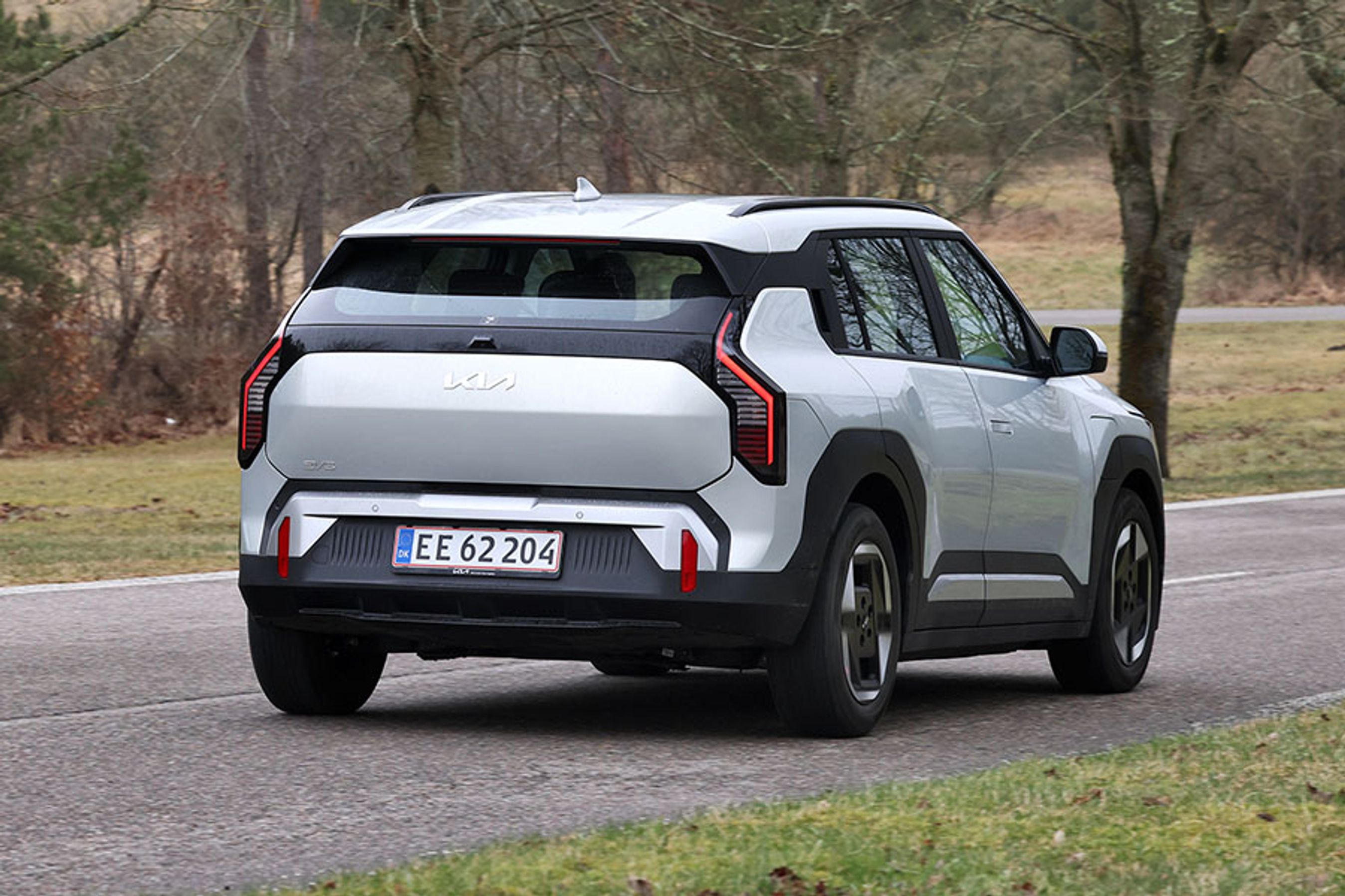 Kia EV3 set skråt bagfra, mens den kører mellem træer på en vej