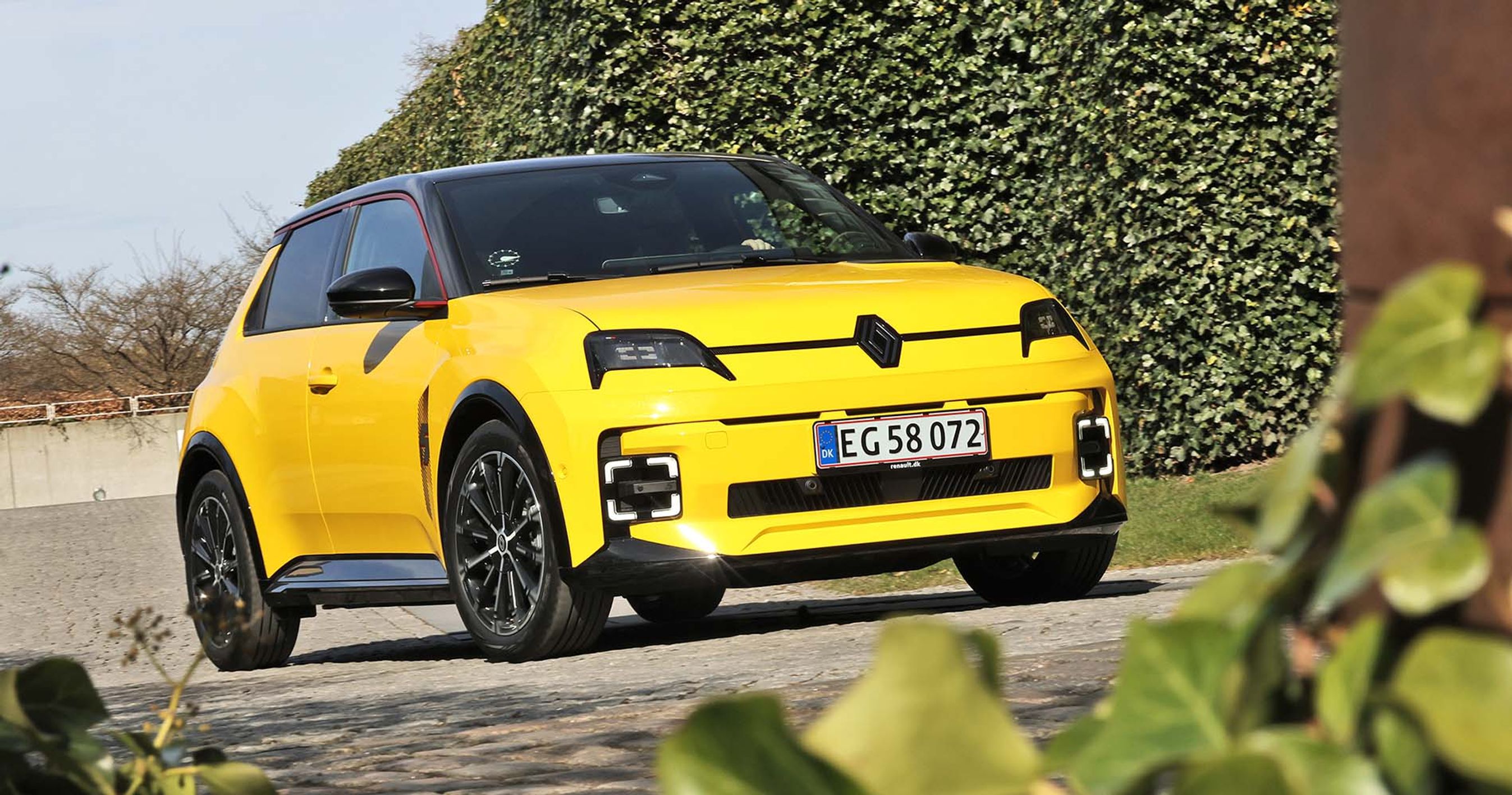 Gul Renault 5 set forfra med buske i forgrunden