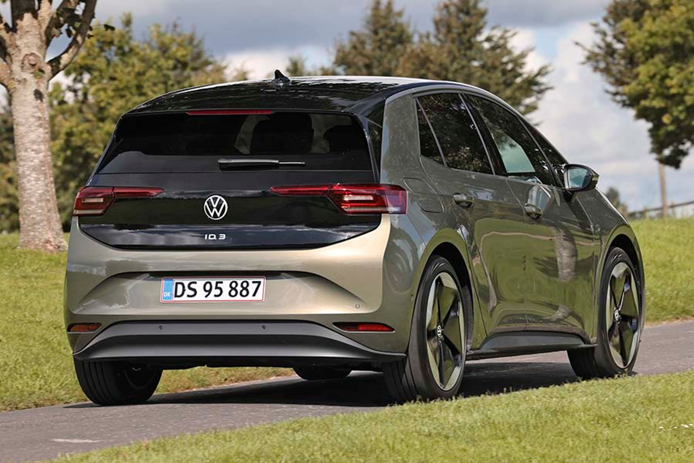 Elbilen VW ID.3 set bagfra, mens den kører på en landevej med græs og træer.